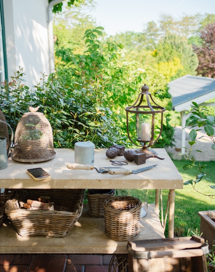 Tuin met stenen tafel, rieten manden, tuingereedschap en lantaarn met kaars