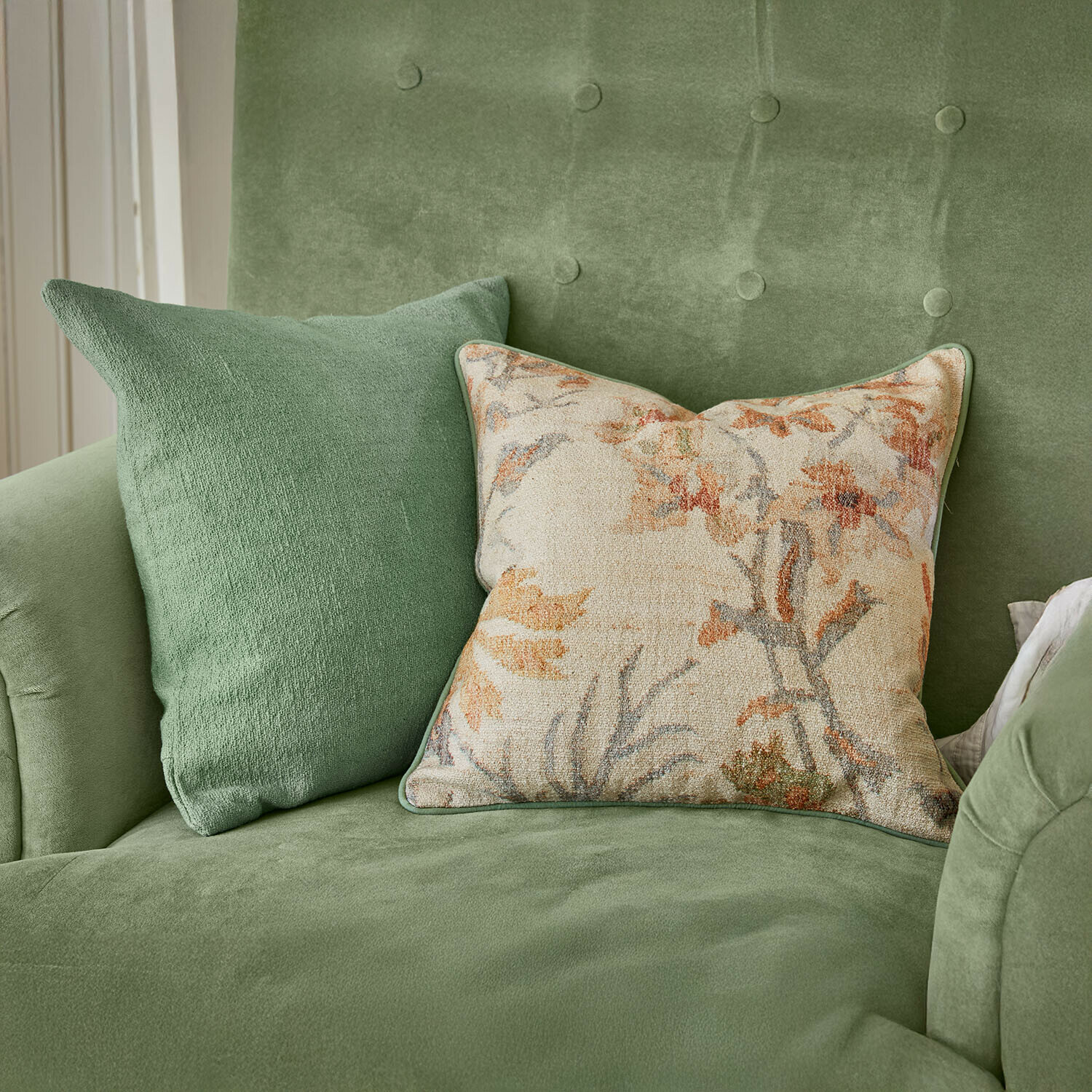 Groene fluwelen bank met twee kussens, één effen en één met bloemenpatroon, stijlvolle woondecoratie