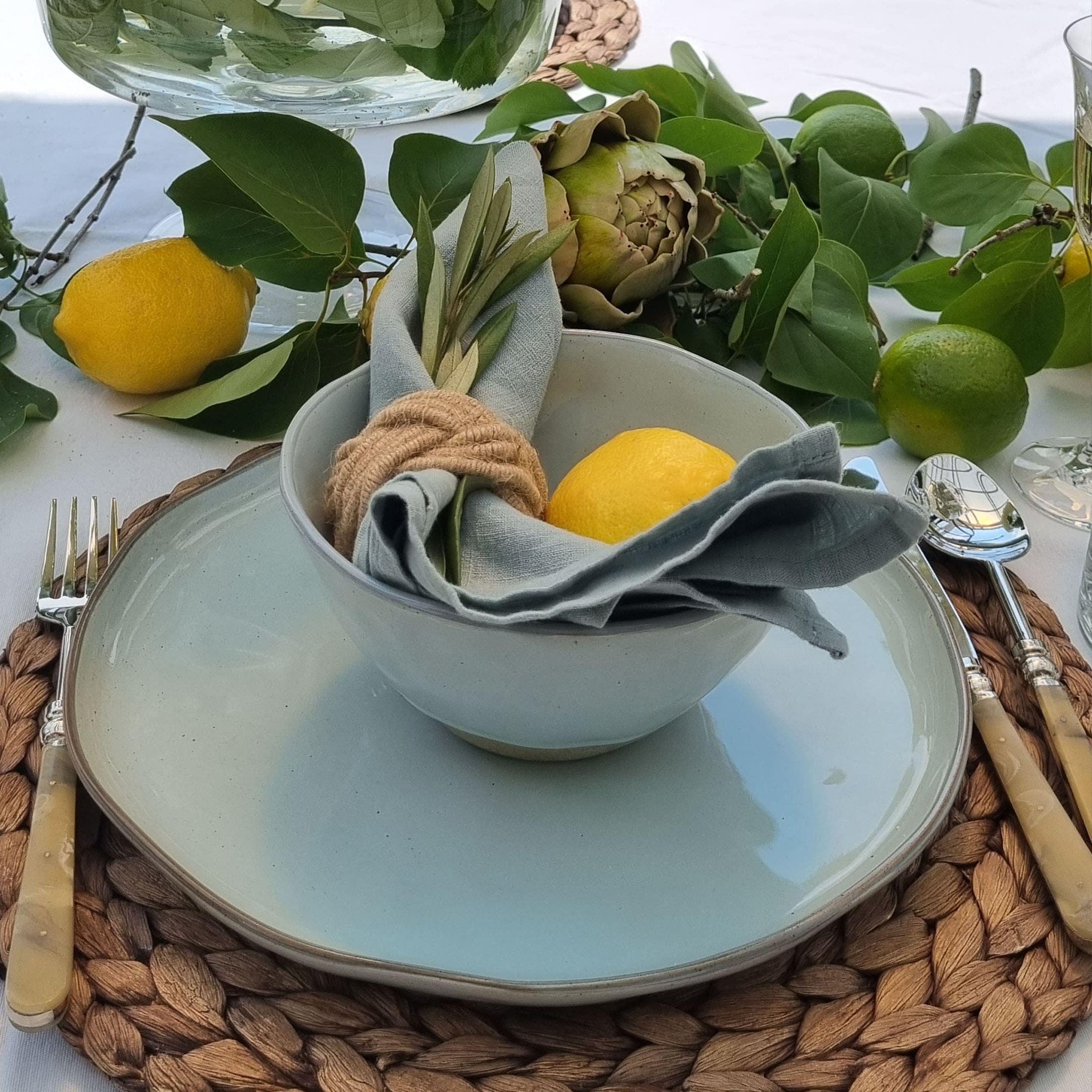 Servies met lichtgekleurde keramische kom en bord op gevlochten onderzetter met citroendecoratie