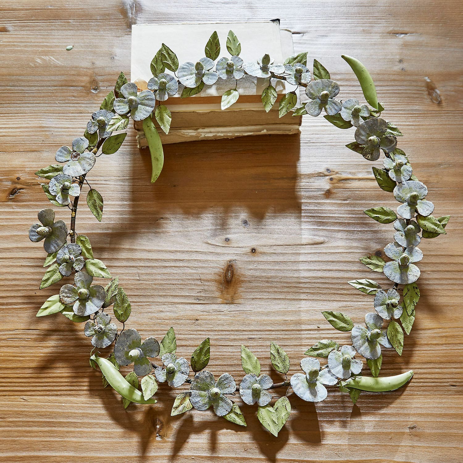 Krans Cecilia Decoratieve metalen krans met groene bladeren en witte bloemen op houten tafel