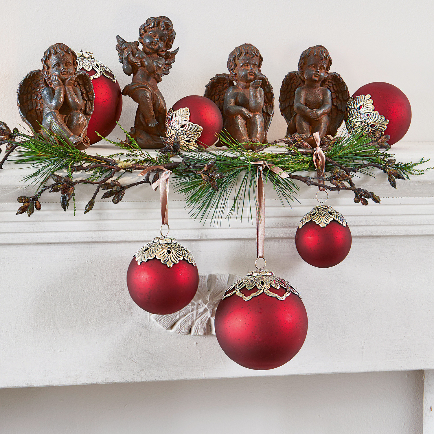 Kerstdecoratie met rode ballen en bruine engelen op een witte schoorsteen