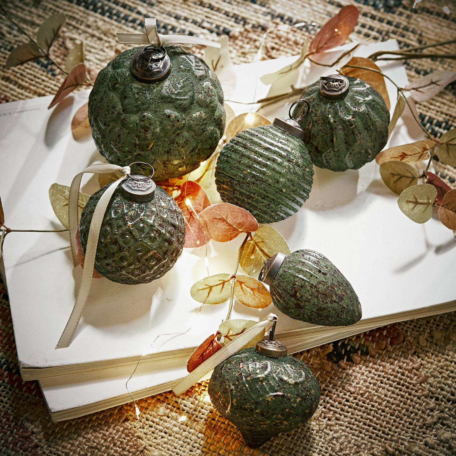 Set groene kerstballen met textuur en linten op wit boek op natuurlijke vloerkleed