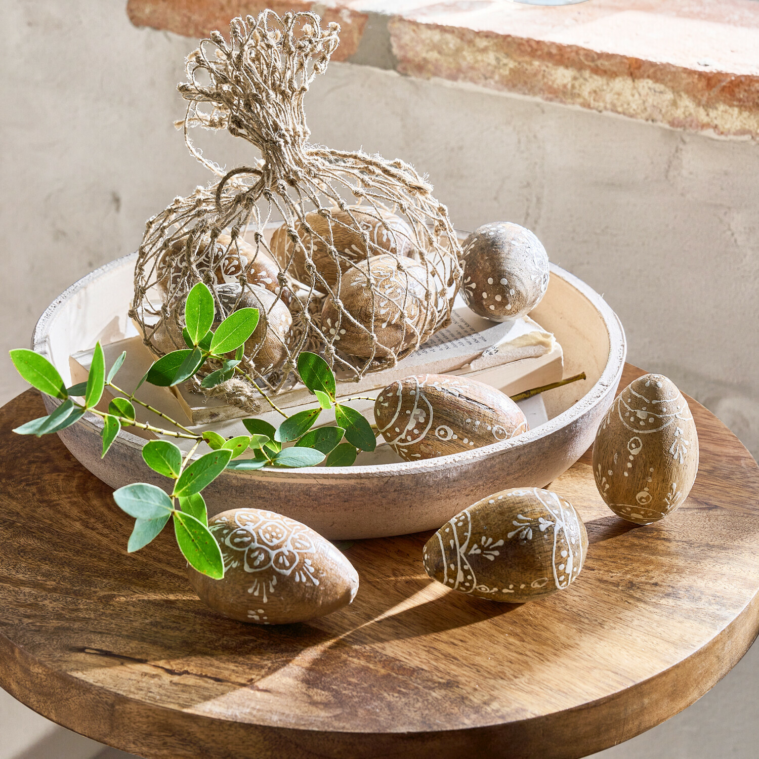 Houten eieren met wit patroon in schaal op houten tafel met groene bladeren als decoratie