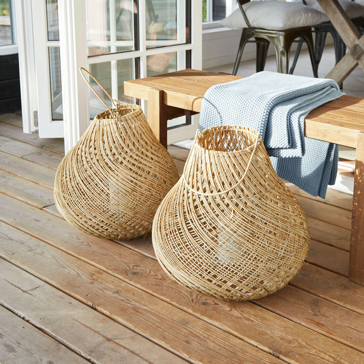 Twee natuurlijke rieten lantaarns op een houten vloer naast een bank met een blauwe deken