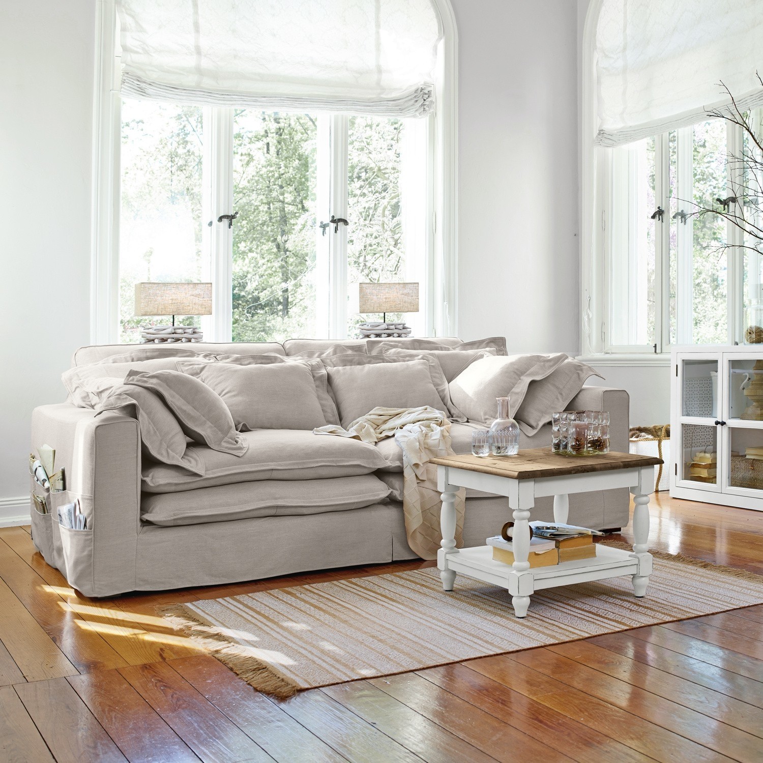 Beige stoffen bank met kussens en witte salontafel op houten vloer in lichte woonkamer