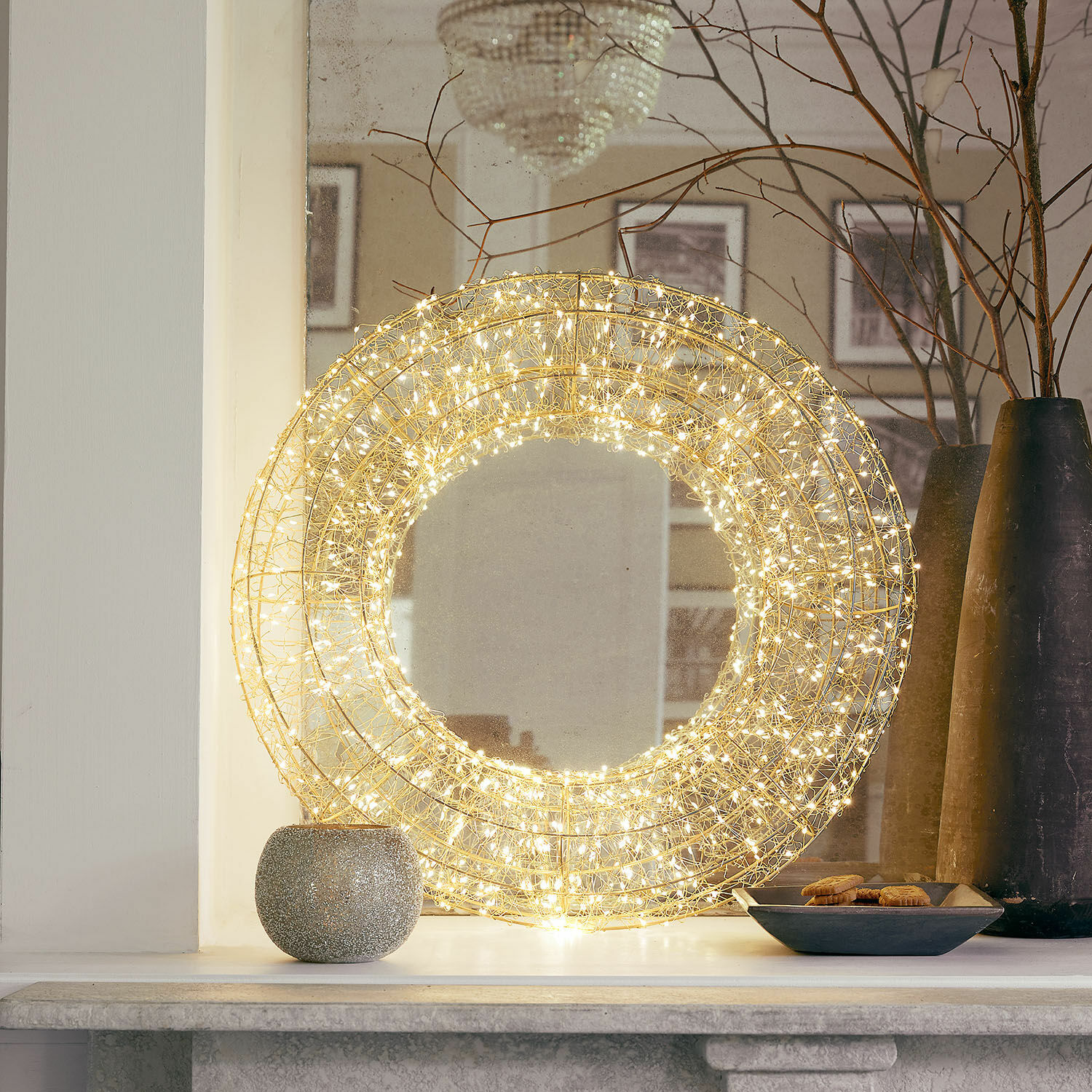 Ronde gouden draaddecoratie met warme LED-lichtjes op de schoorsteenmantel