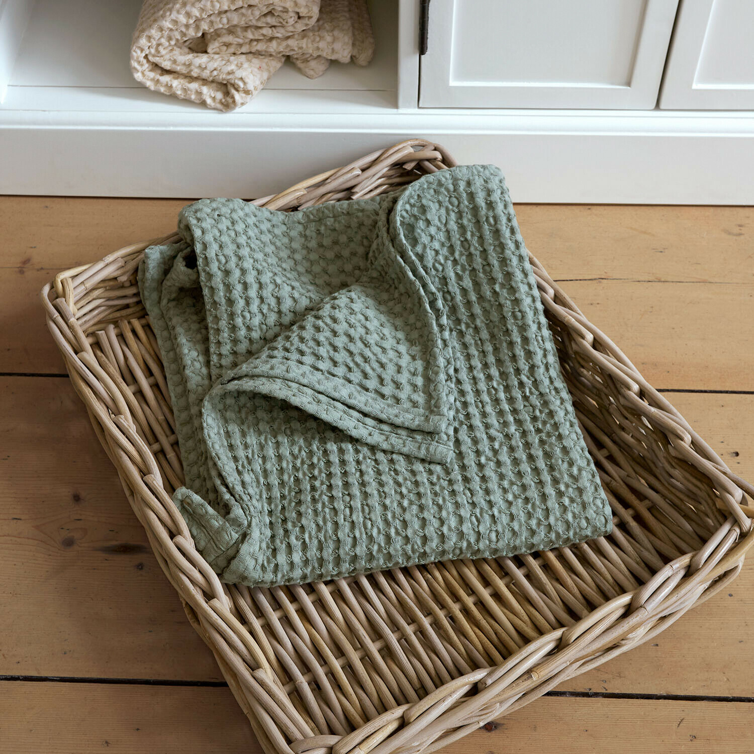 Handdoek Maralei Zachte groene katoenen deken met wafelstructuur in een rieten mand op een houten vloer