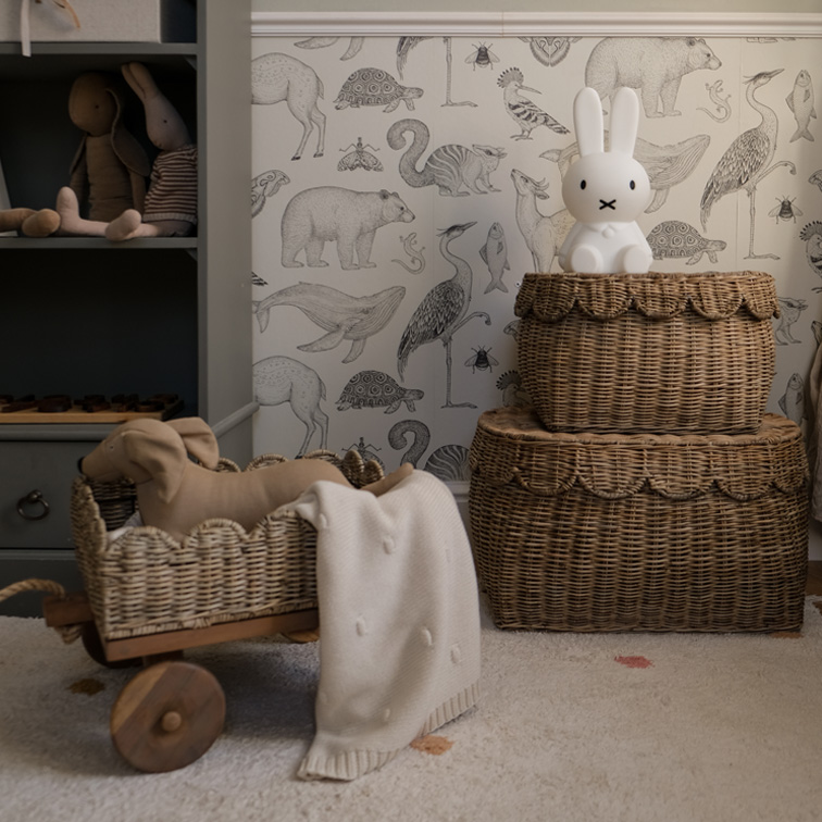 Twee bruine rieten manden met konijnenlamp en speelgoed in kinderkamer met dierenbehang