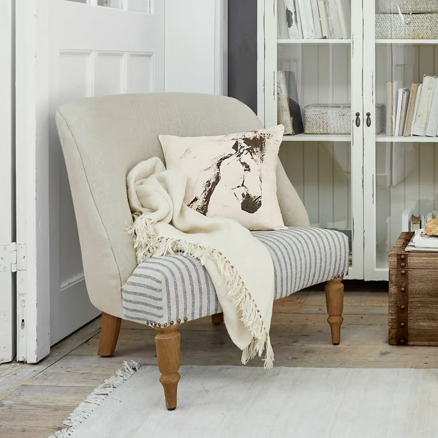 Tweekleurige gestoffeerde bank met houten poten, kussen met paardenafbeelding en crème deken