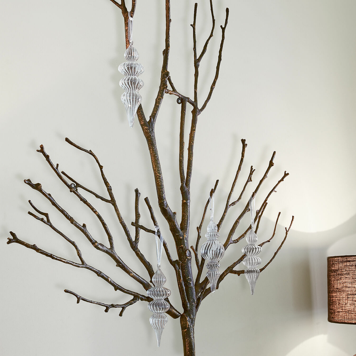 Transparante versieringen hangen aan donkere takken tegen een lichte achtergrond, interieurdecoratie