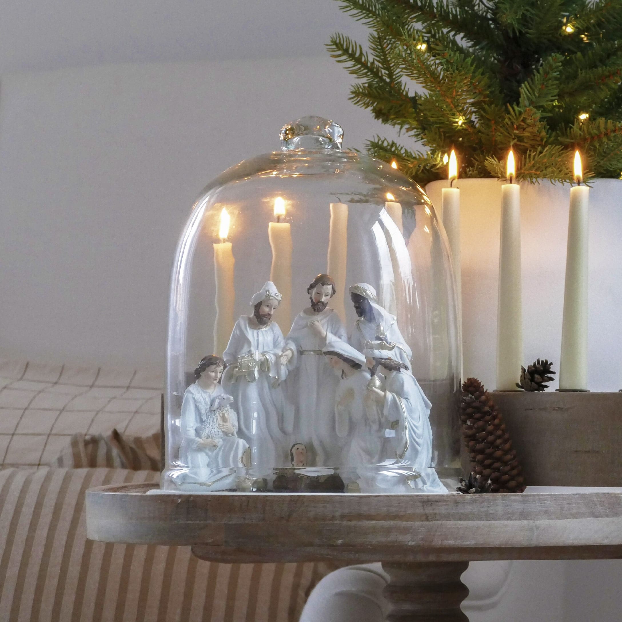 Witte keramische kerststal onder glazen stolp met brandende kaarsen en feestelijke decoratie