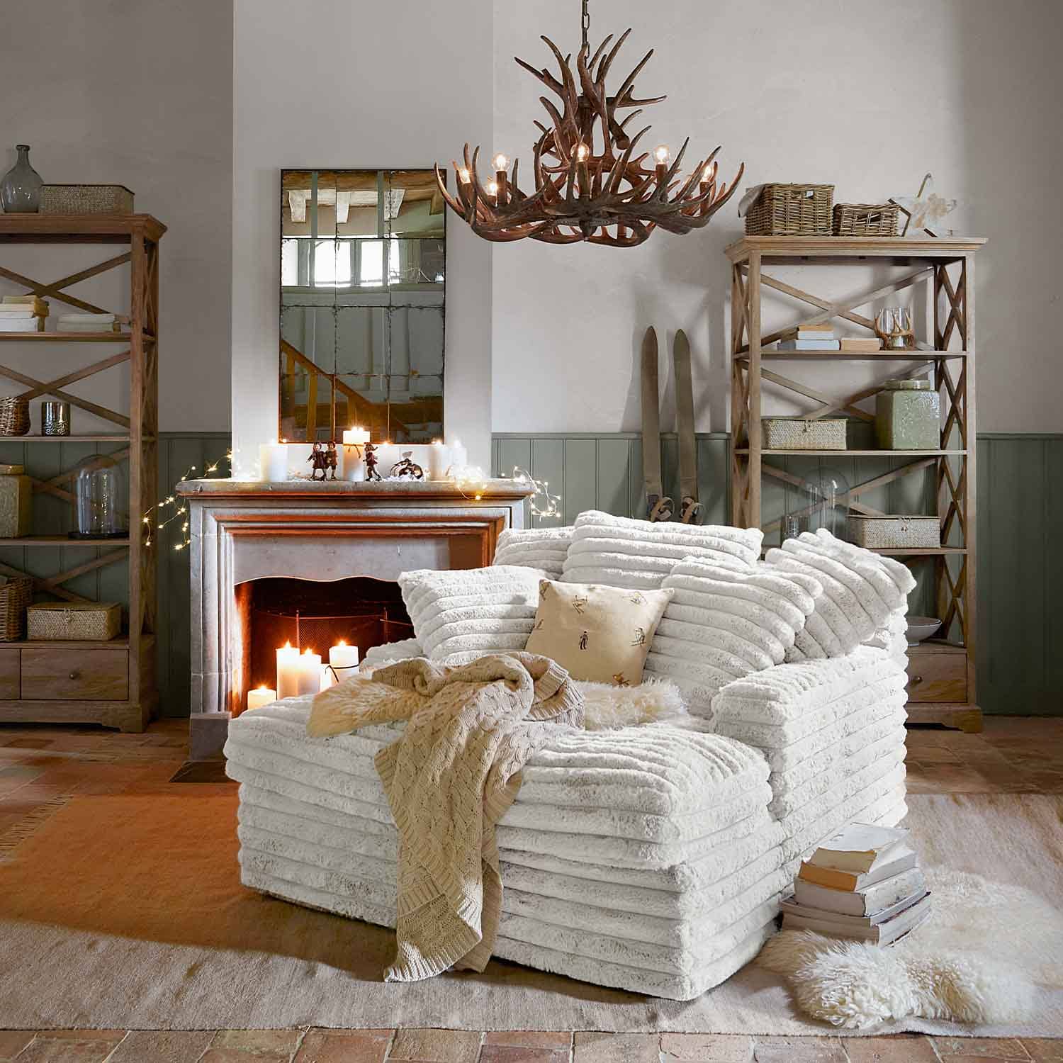 Gezellige witte fauteuil van zacht materiaal in rustieke woonkamer met open haard en houten planken