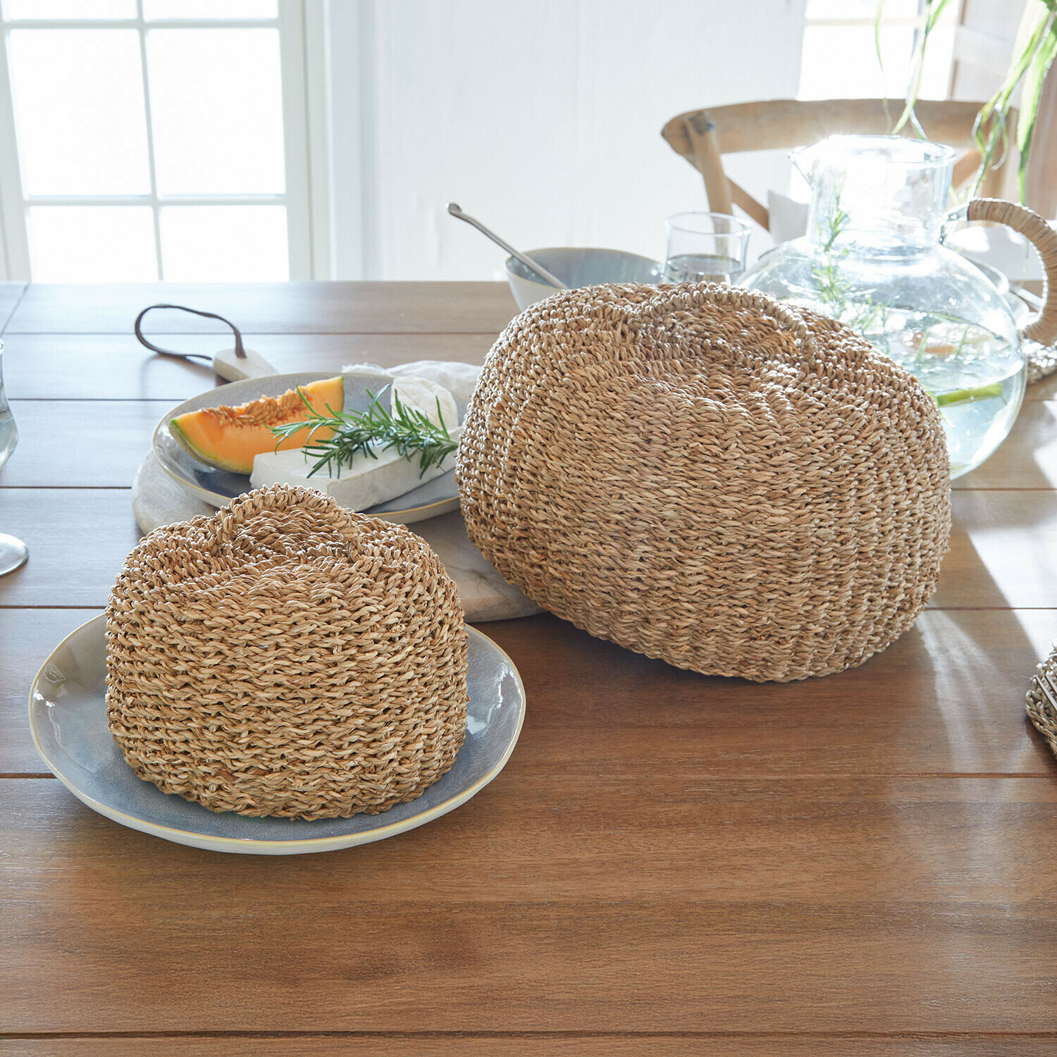 Twee ronde broodkappen van gevlochten natuurlijk materiaal in beige op een lichte houten tafel