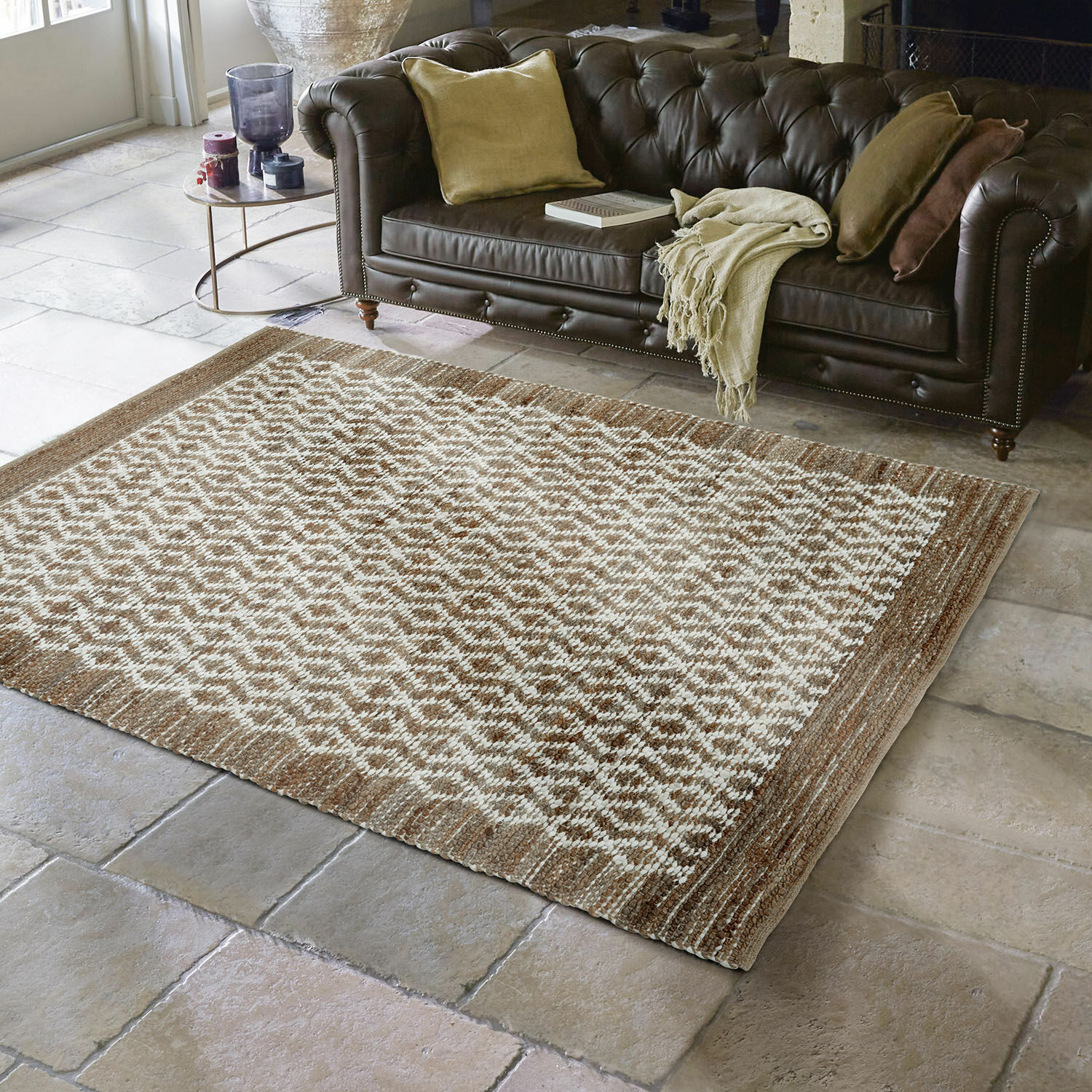 Bruin-crèmekleurig vloerkleed met geometrisch patroon op stenen vloer voor een donkere leren bank in woonkamer