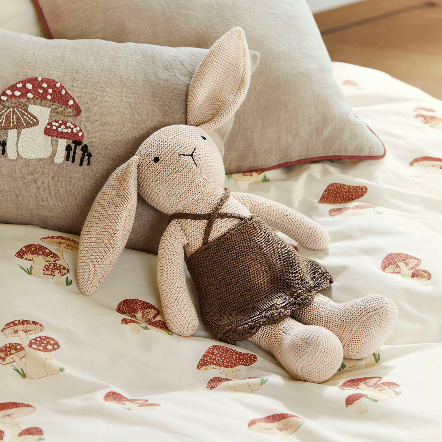 Zacht speelgoed Flicka Beige gebreide konijn met bruine jurk op beddengoed met paddenstoelenprint, decoratief kussen met paddenstoelen