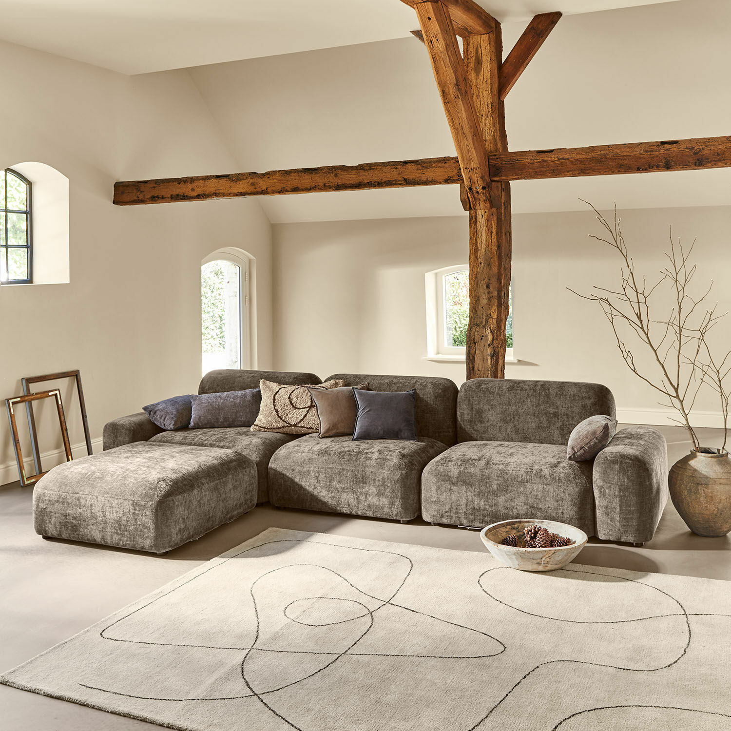 Grijze modulaire stoffen bank in moderne woonkamer met houten balken en lichte vloerkleed