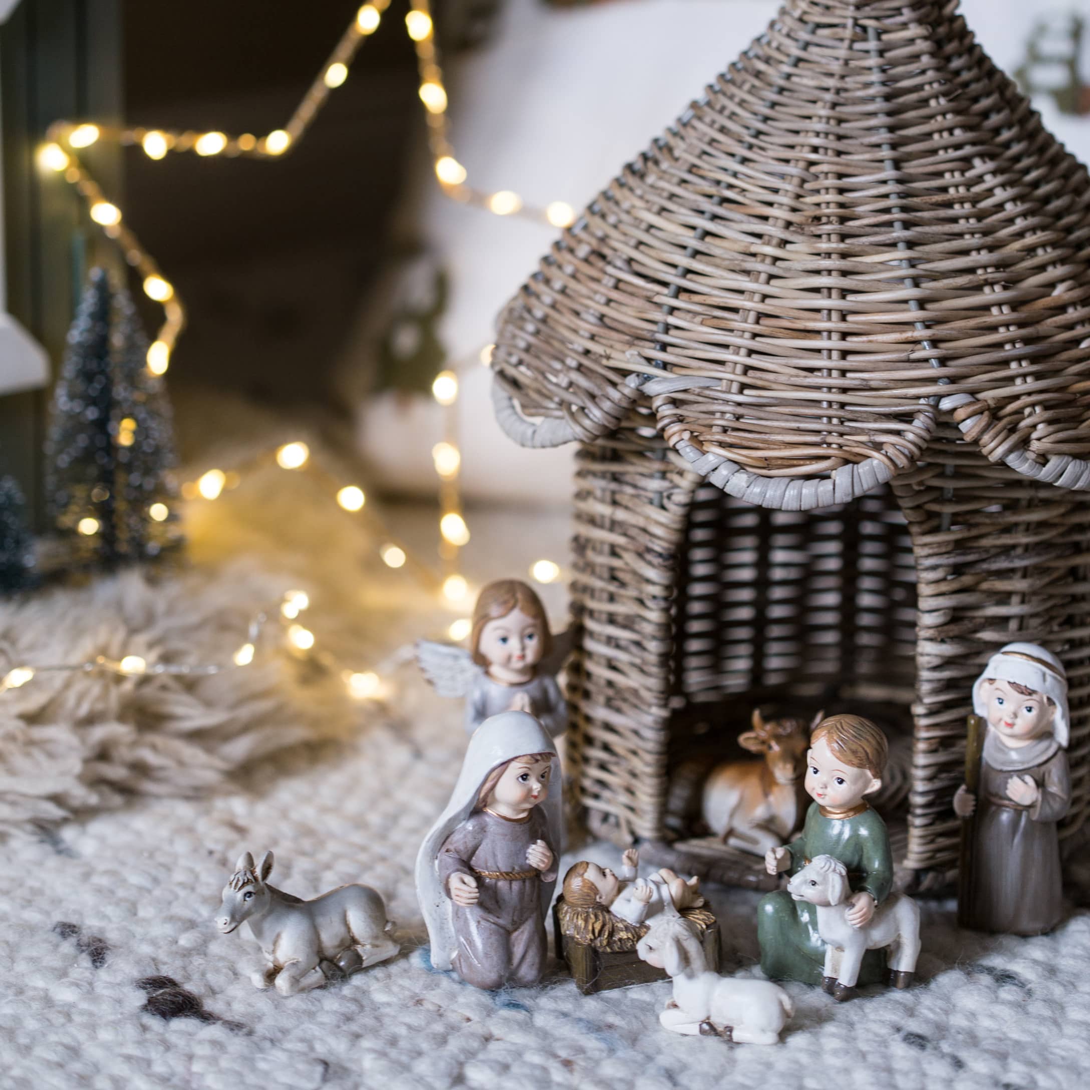 Kerststalfiguren met een rieten huisje en figuren op een zachte mat met LED-lichtjes