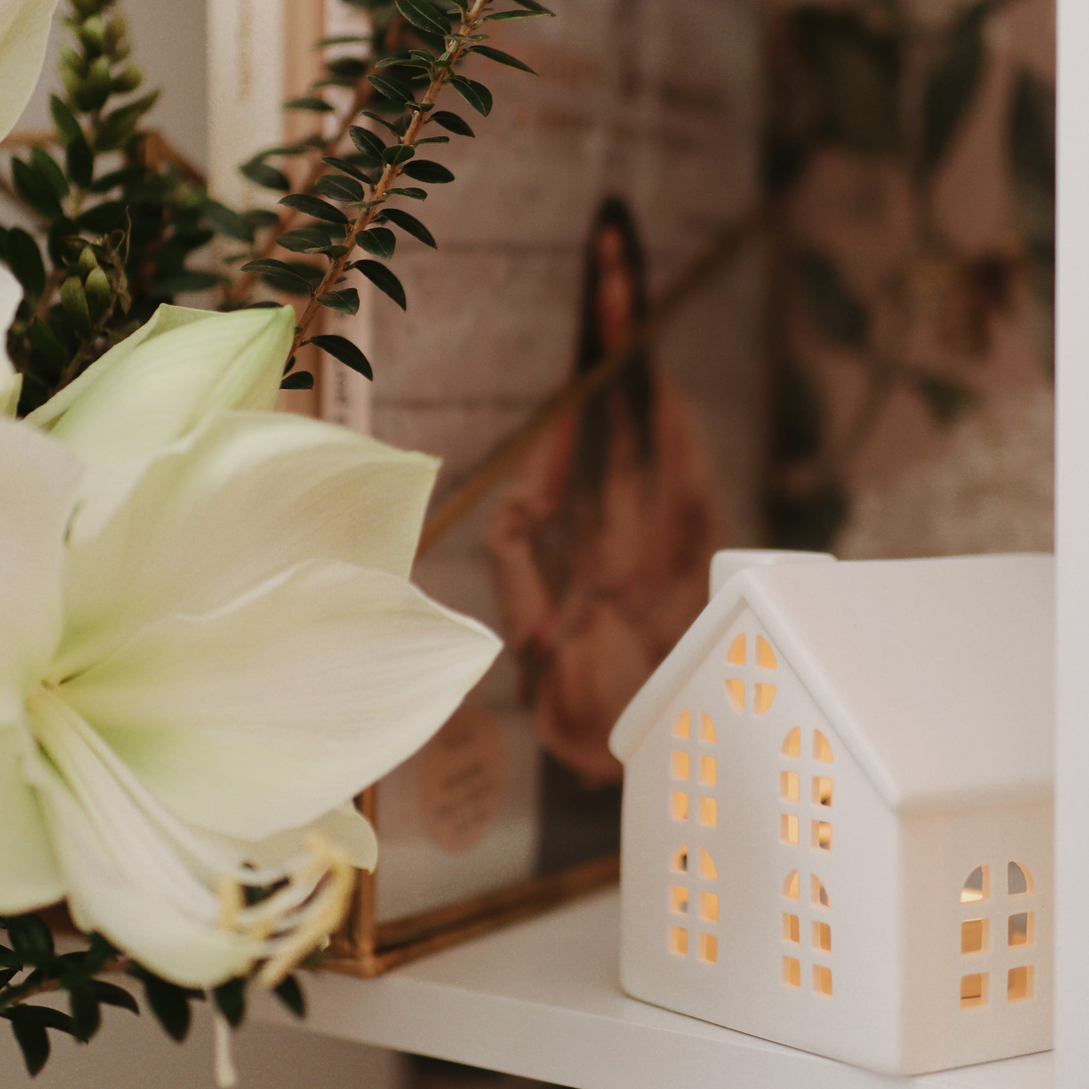 Witte keramische huisdecoratie met verlichting op plank naast witte bloem en groene bladeren