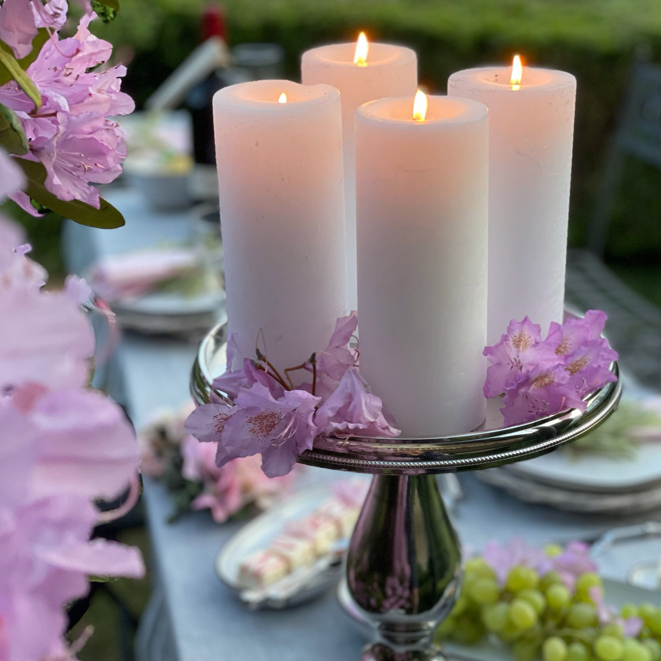 Vier witte kaarsen op zilveren kandelaar met roze bloemen op een tuintafel