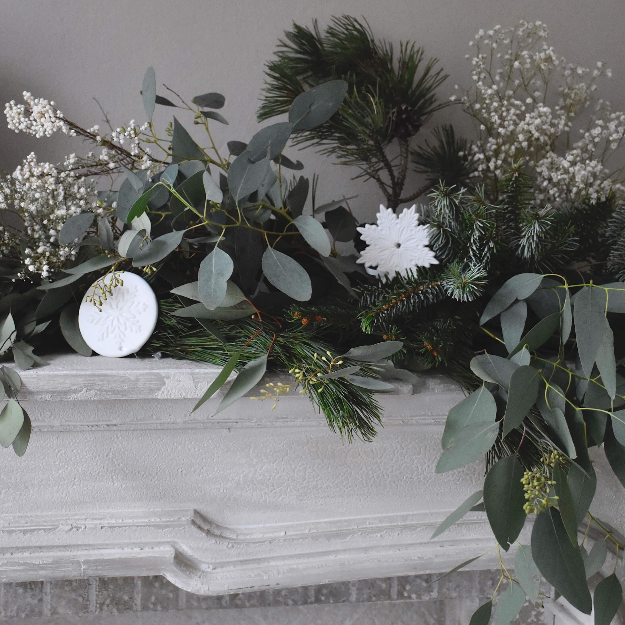 Decoratieve krans van groene takken en witte sneeuwvlokornamenten op een witte stenen open haard