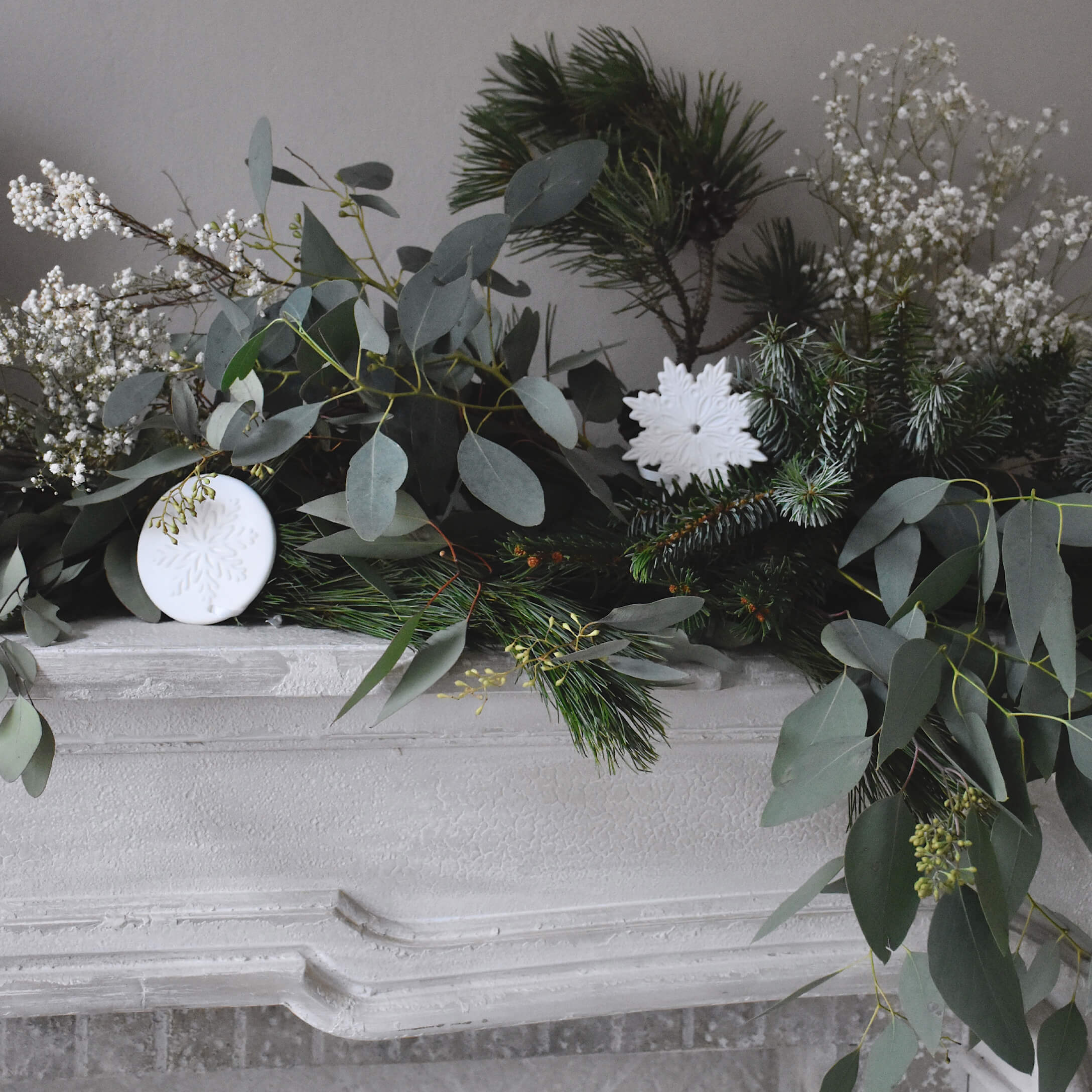 Decoratieve krans van groene takken en witte sneeuwvlokornamenten op een witte stenen open haard