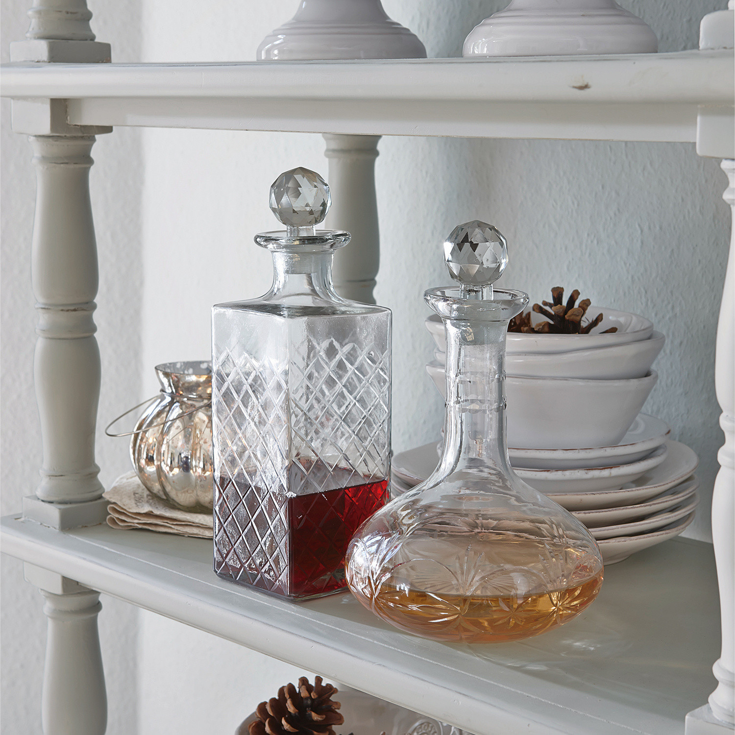 Glazen karaf met kristallen stop op witte plank met rode en amberkleurige drank