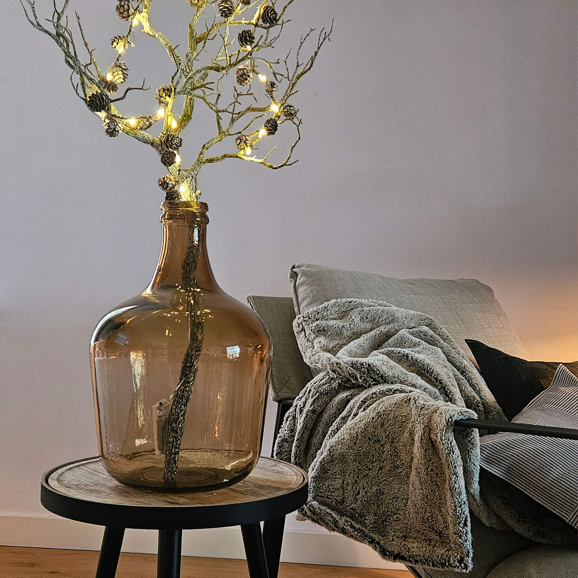 Bruine glazen fles met verlichte tak op houten bijzettafel in woonkamer
