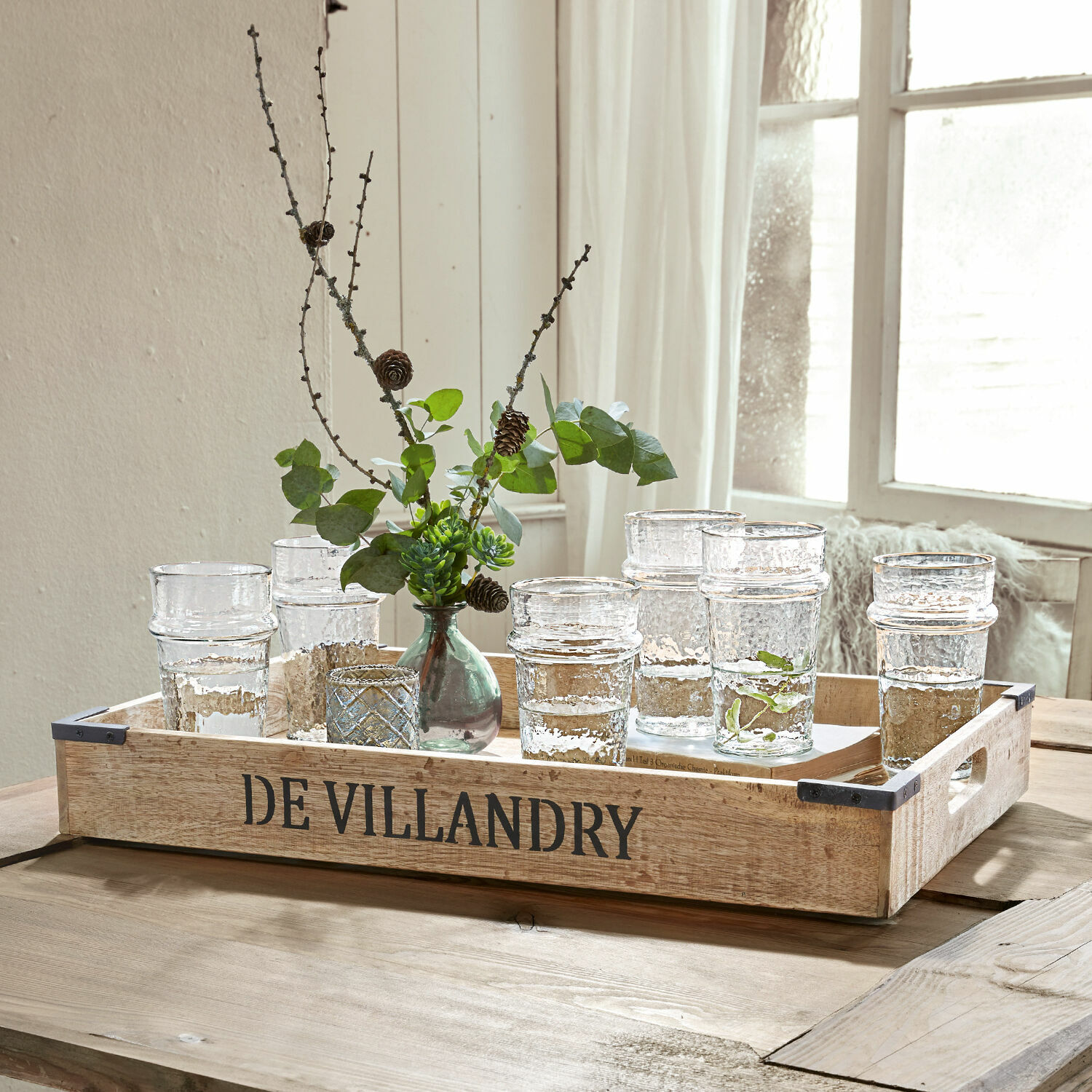 Dienblad Villandry Houten dienblad DE VILLANDRY met heldere glazen en groene takken op lichte houten tafel