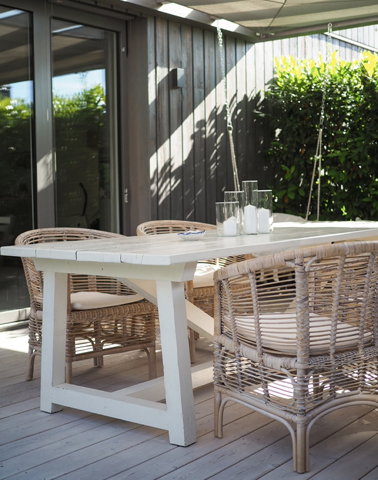 Witte houten tuintafel met natuurlijke rotan stoelen op zonnig buitenterras