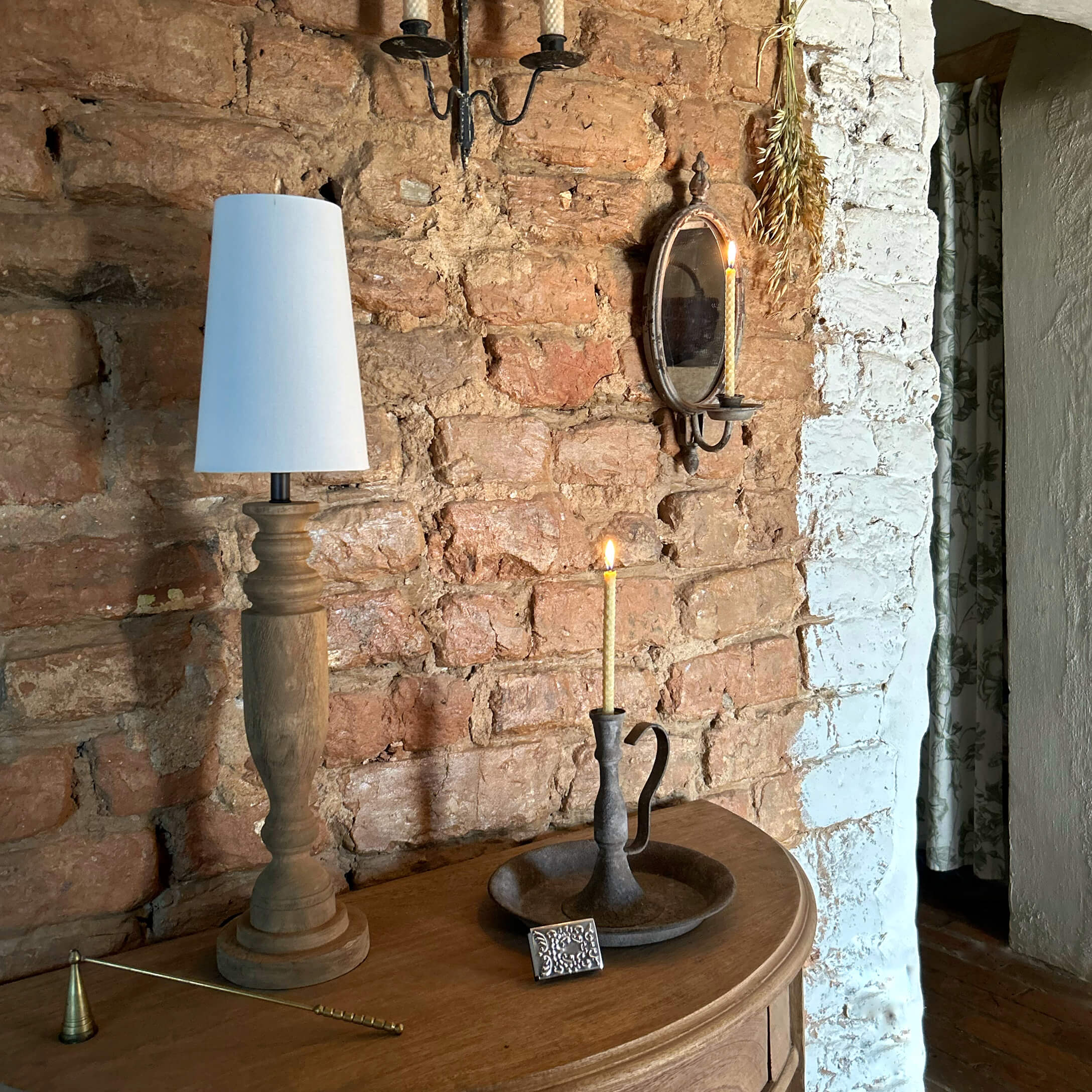 Houten lamp met witte kap en metalen kandelaar met brandende kaars op houten tafel bij bakstenen muur