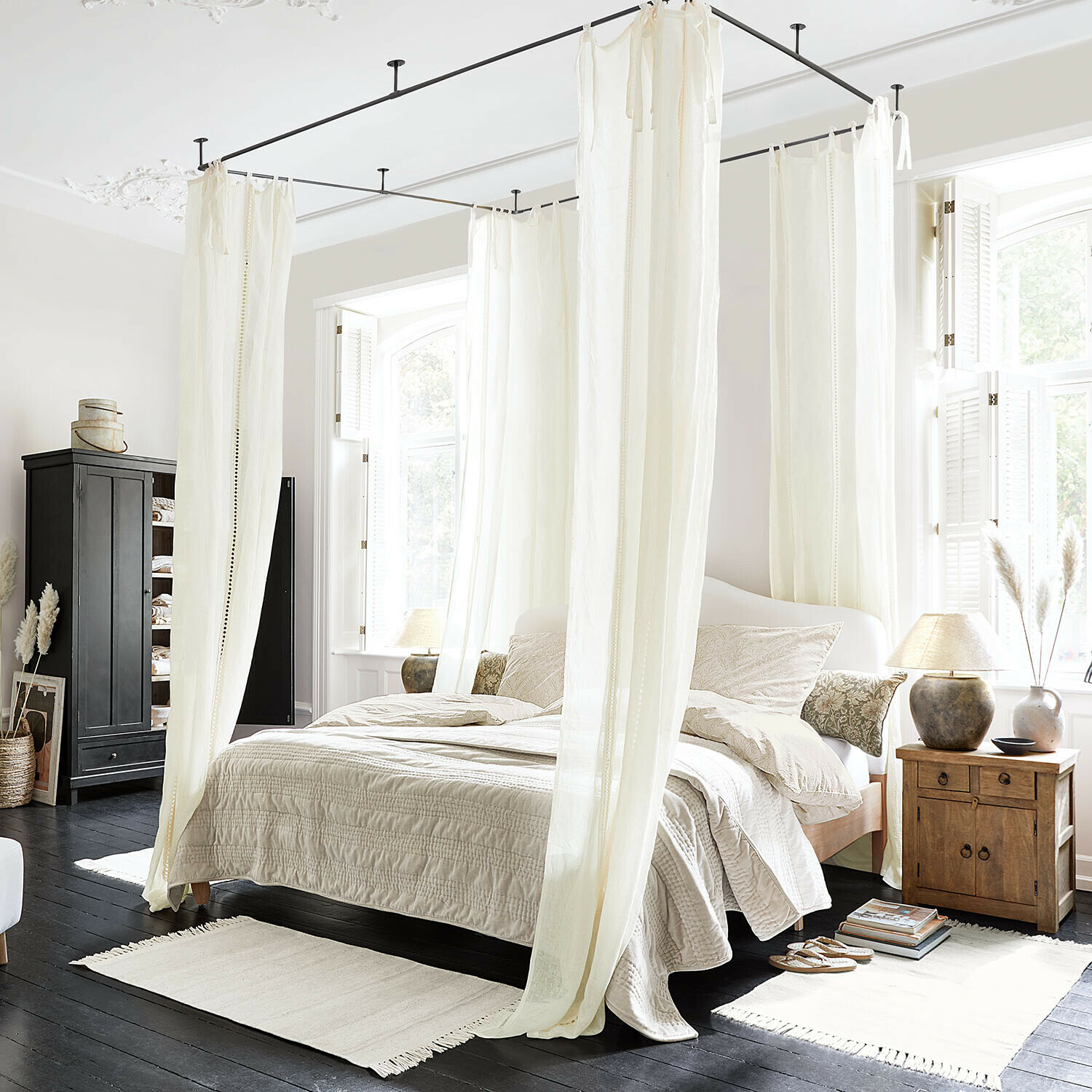 Slaapkamer met wit katoenen hemelbed en beige beddengoed op donkere houten vloer, natuurlijk licht