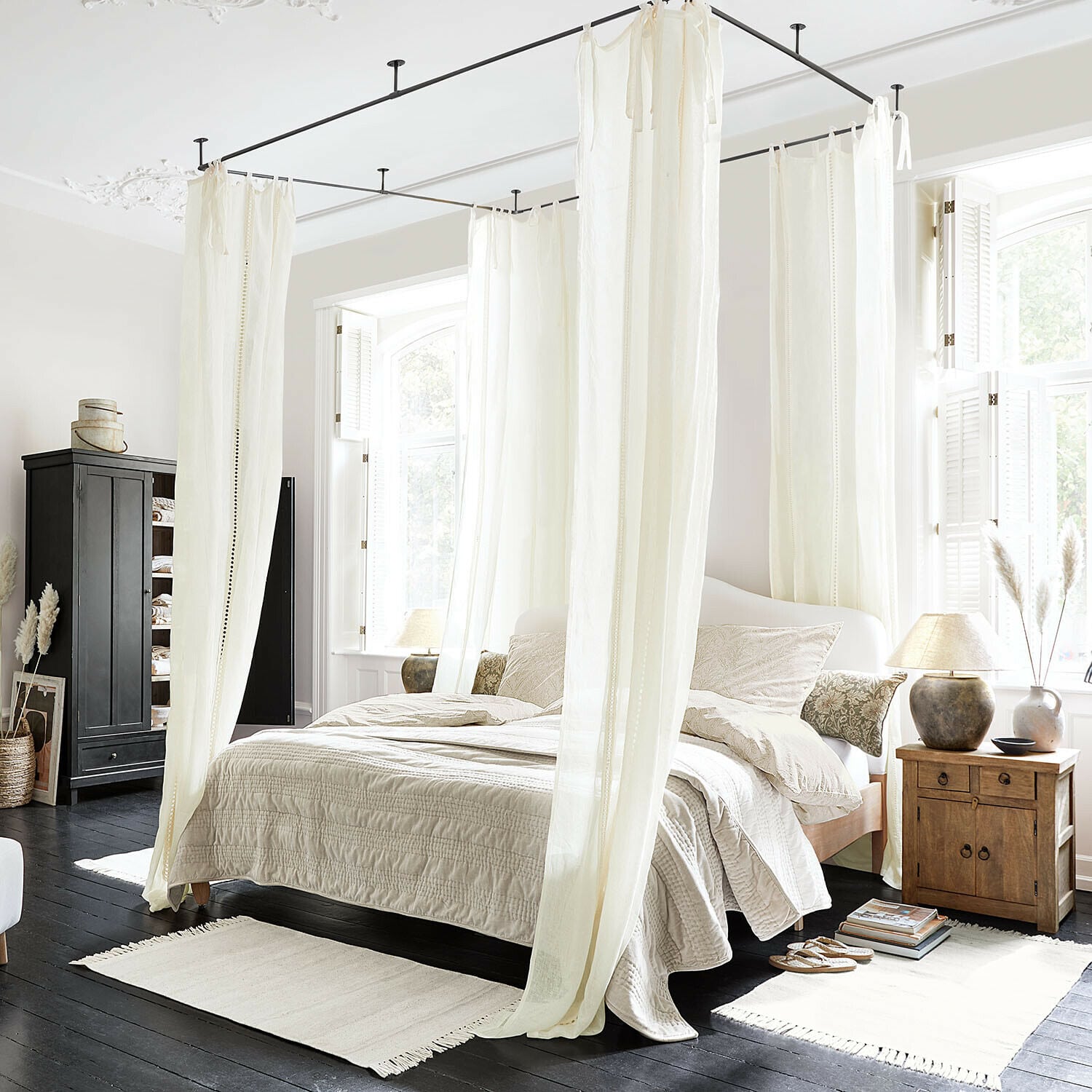 Gordijn Elorine Slaapkamer met wit katoenen hemelbed en beige beddengoed op donkere houten vloer, natuurlijk licht