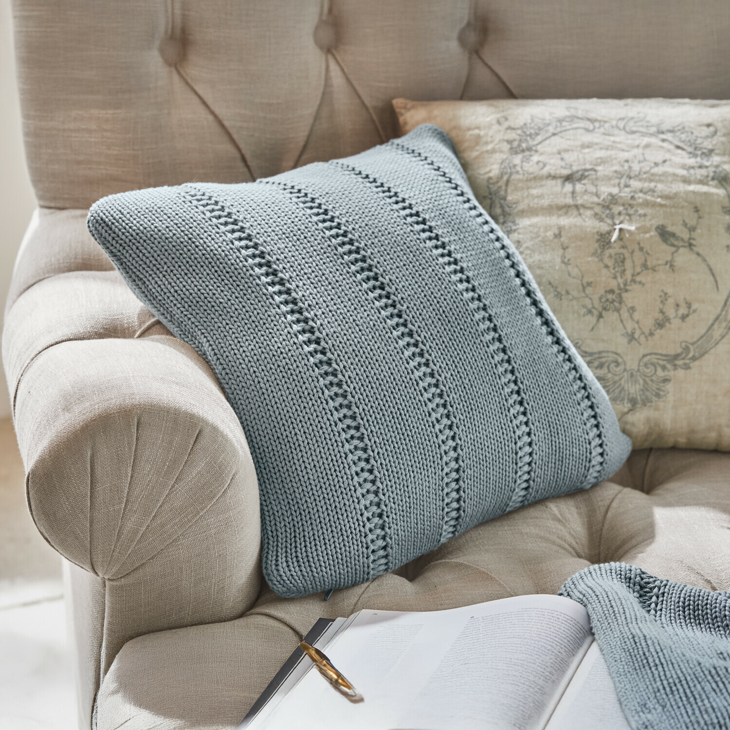 Kussenhoes Lémeré Beige gestoffeerde fauteuil met doorgestikte rugleuning, grijze gebreide deken en kussen