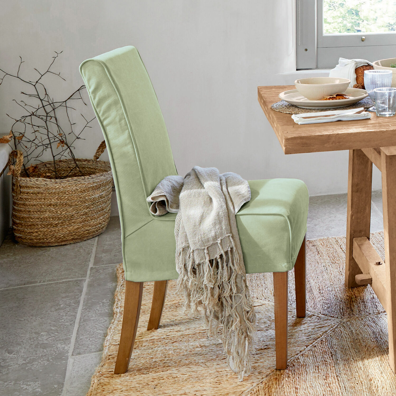 Lichtgroene gestoffeerde stoel met houten poten en beige deken in lichte eetkamer