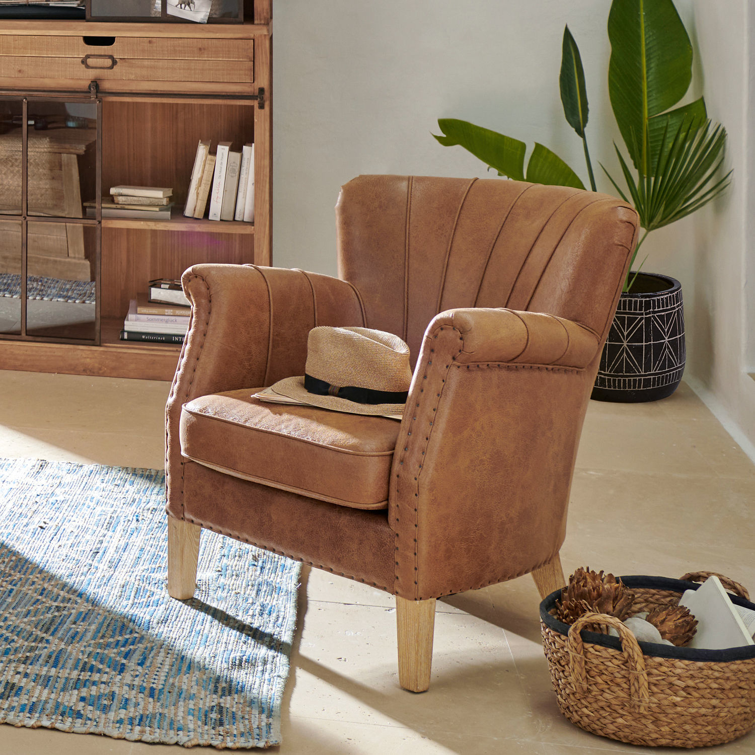 Bruine fauteuil van kunstleer met houten poten in gezellige kamer met vloerkleed en plant