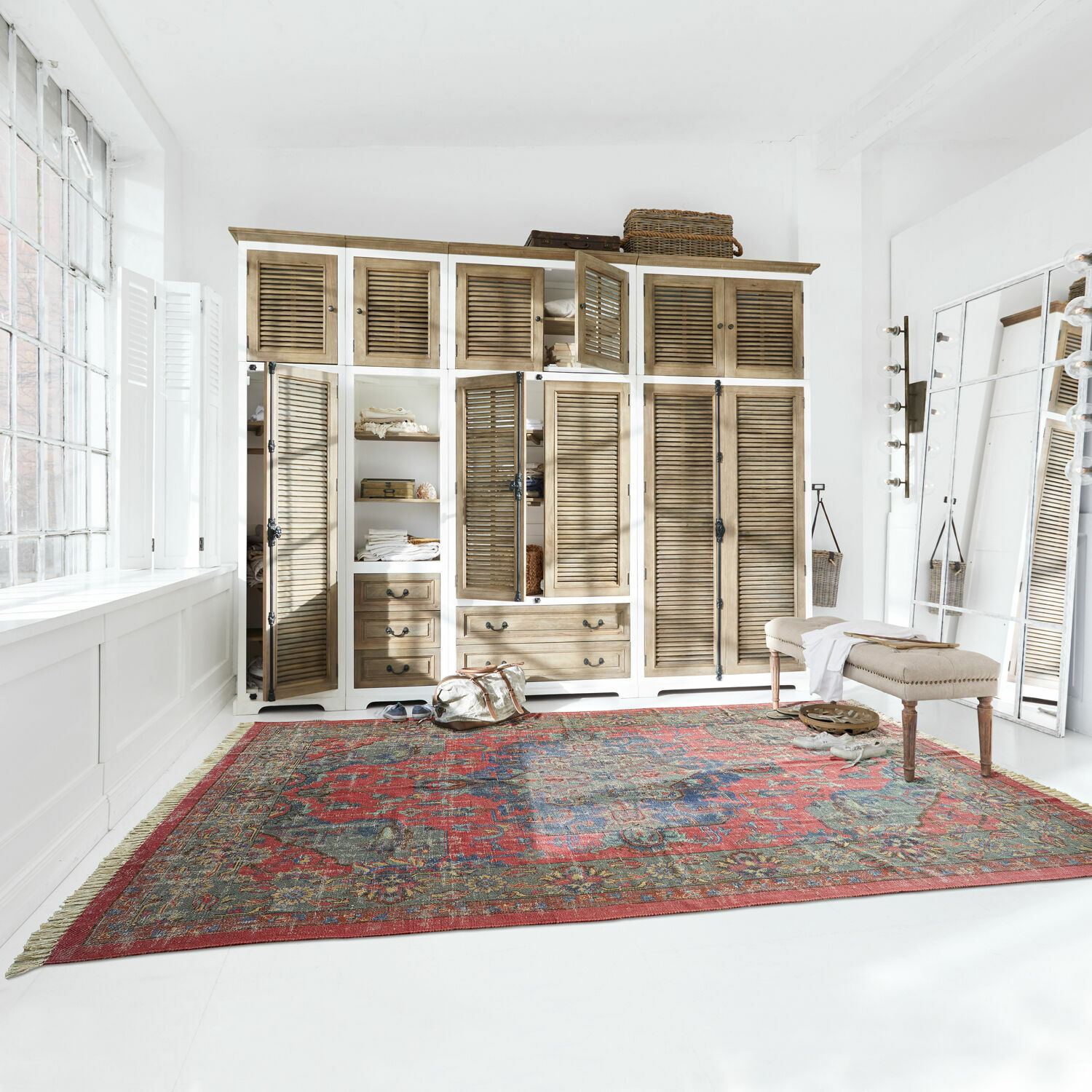 Grote rode vloerkleed met oosters patroon in lichte kamer met houten kast en bankje