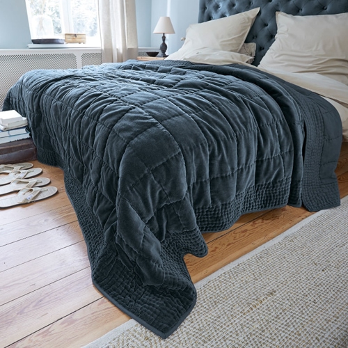 Donkergrijze gewatteerde deken van zacht materiaal op bed in lichte slaapkamer, interieurdecoratie