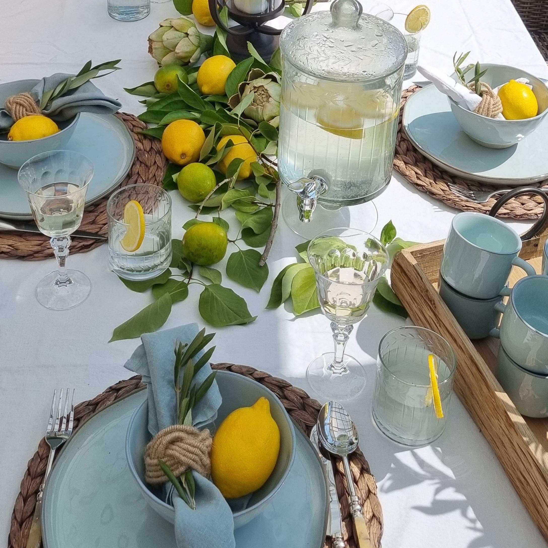 Zomerse tafel met blauw servies, citroenen en groene bladeren op wit tafelkleed, tafeldecoratie