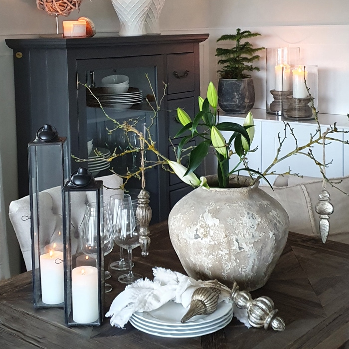 Decoratieve tafel met grote beige keramische vaas en kaarsen in glazen lantaarns