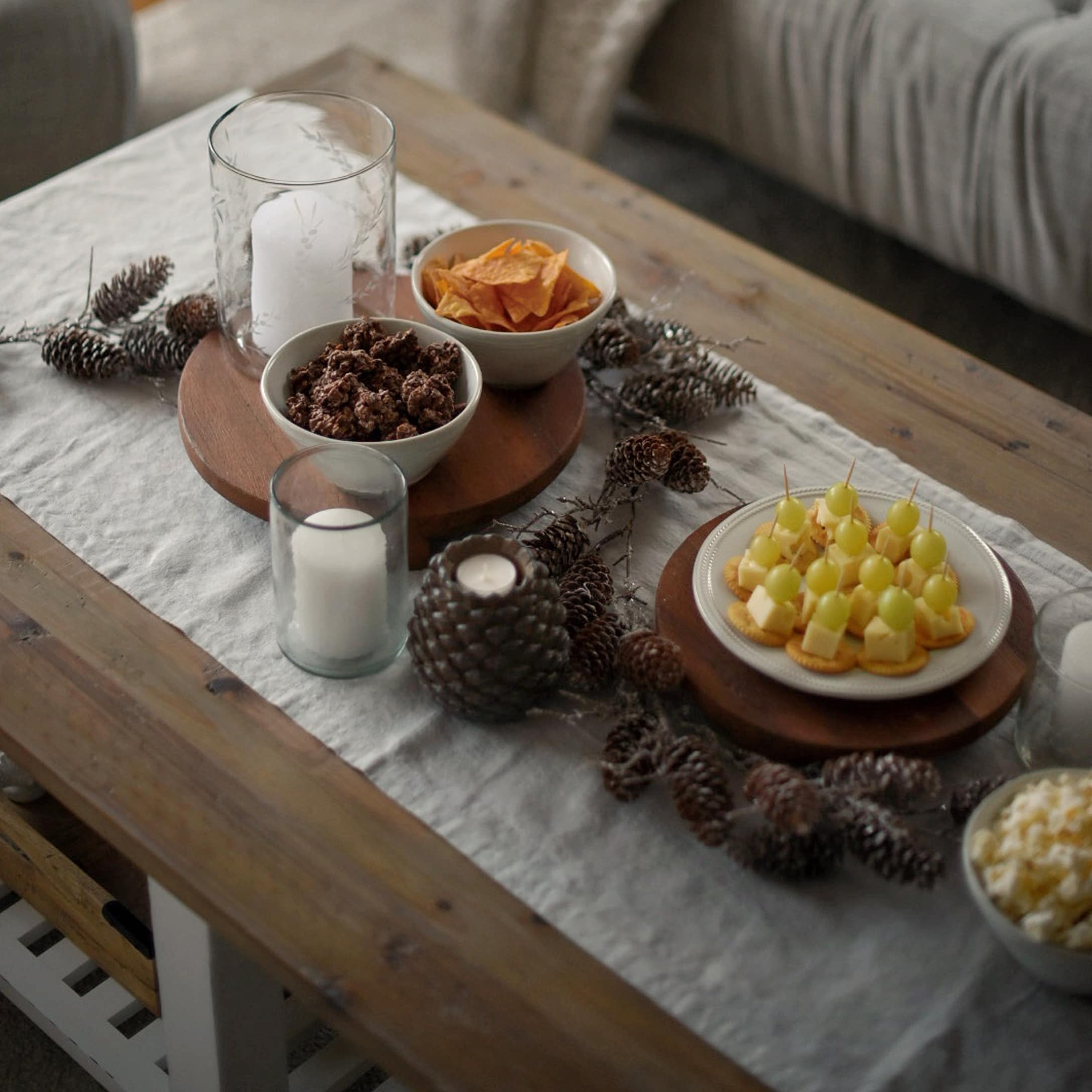 Houten dienblad met snacks en kaarsen op linnen tafelloper met dennenappeldecoratie