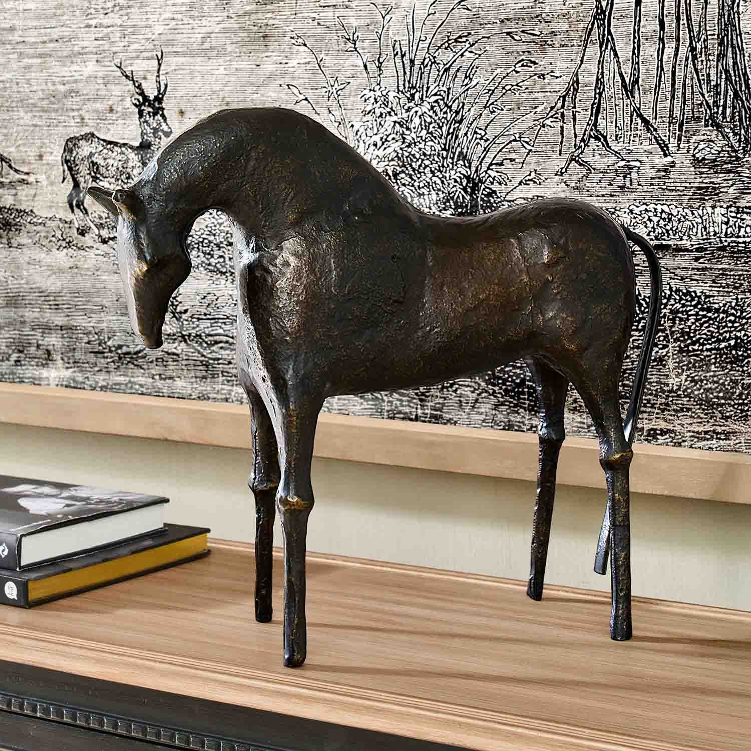 Donkere metalen paardenbeeld op houten blad met boeken als decoratie in interieur