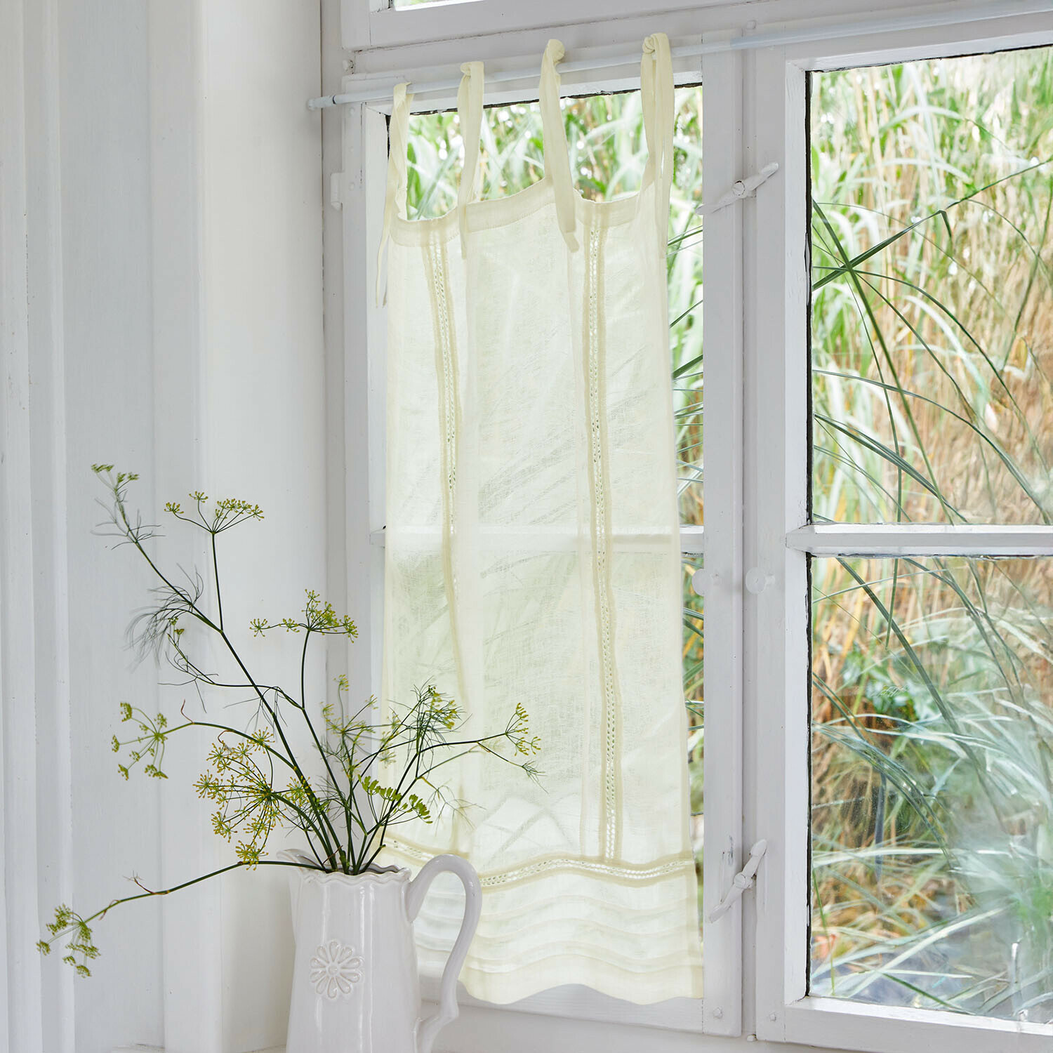 Crèmekleurig gordijn van lichte stof met decoratieve banden aan wit raam, interieurdecoratie