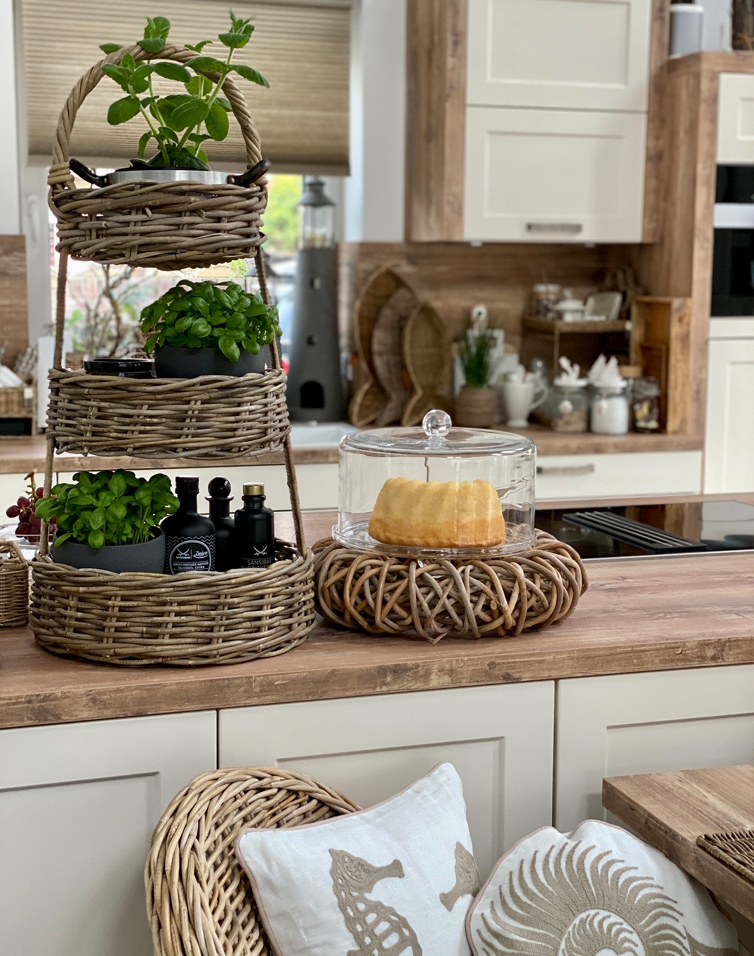 Driedelige rieten standaard met groene planten en glazen stolp voor cake op houten keukenblad