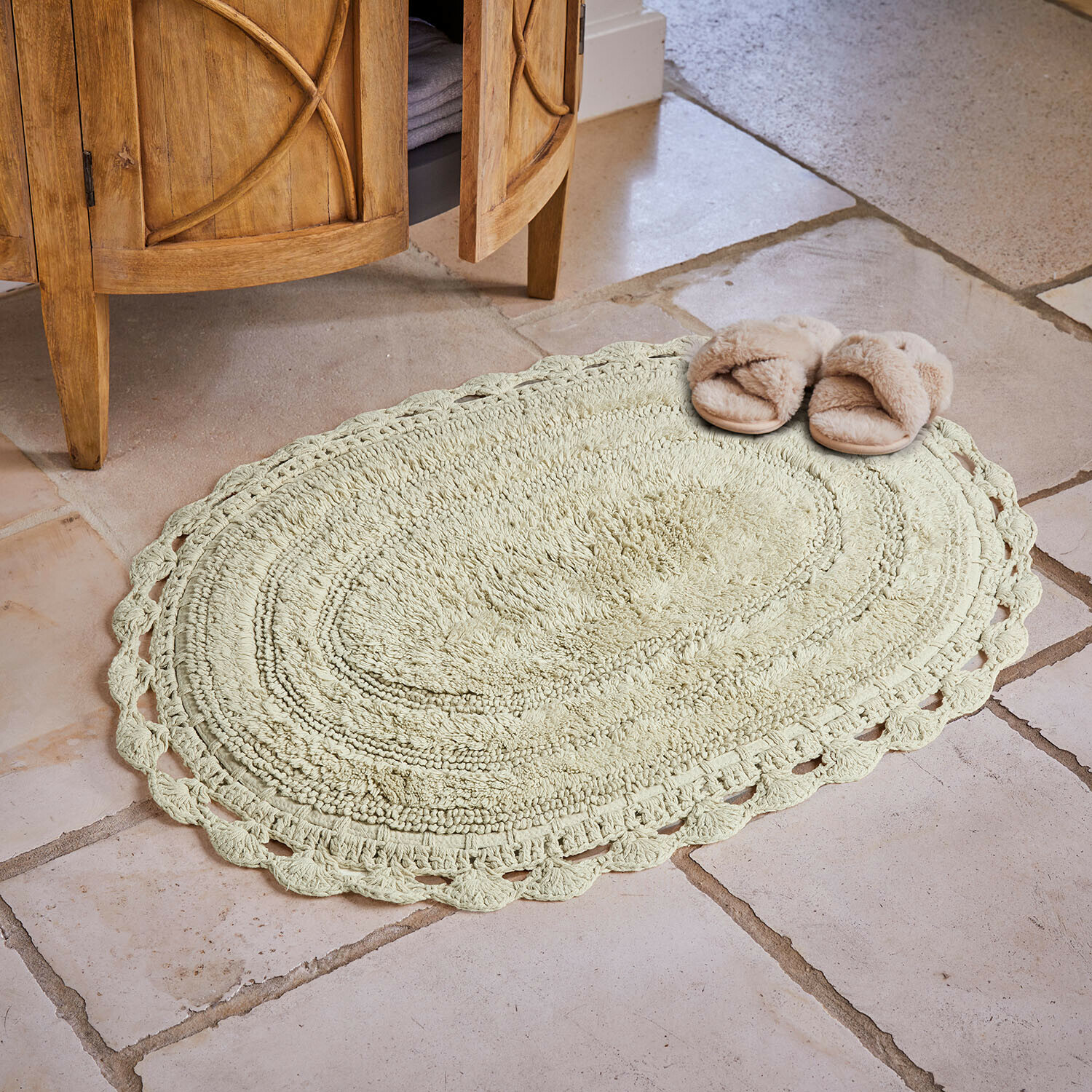 Ovale katoenen vloerkleed in lichtbeige met decoratieve rand op stenen vloer