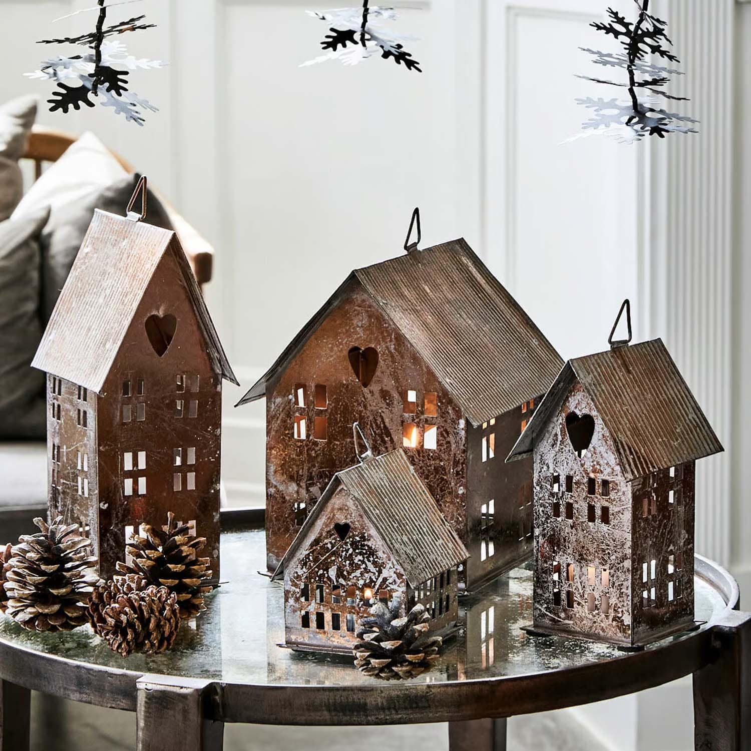 Decoratieve metalen huisjes met uitgesneden harten en ramen op glazen tafel met dennenappels
