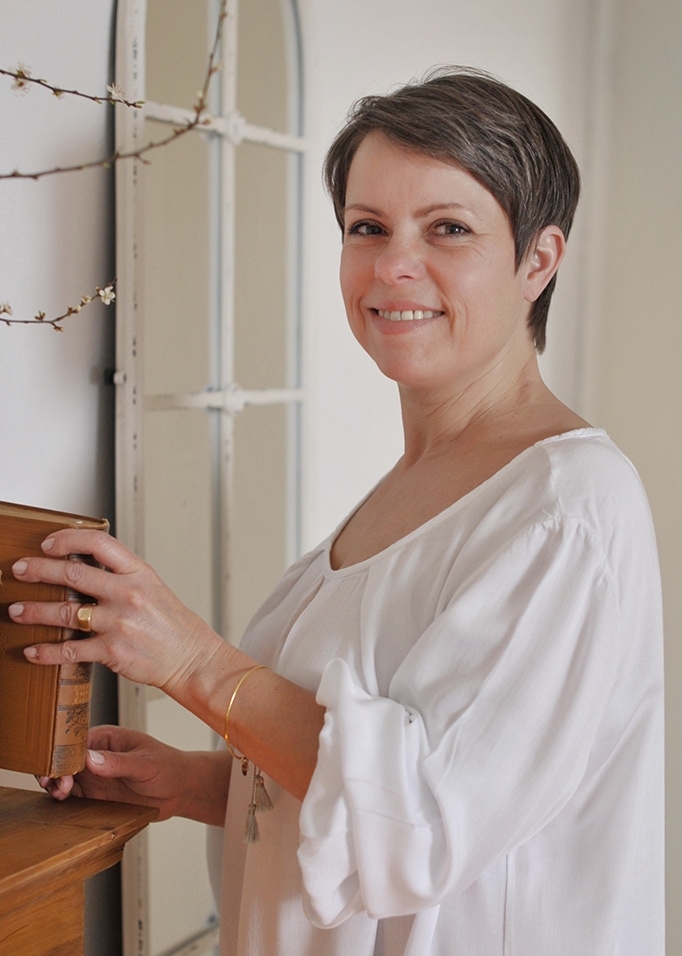 Vrouw in witte katoenen blouse houdt oud boek vast bij houten plank in lichte kamer