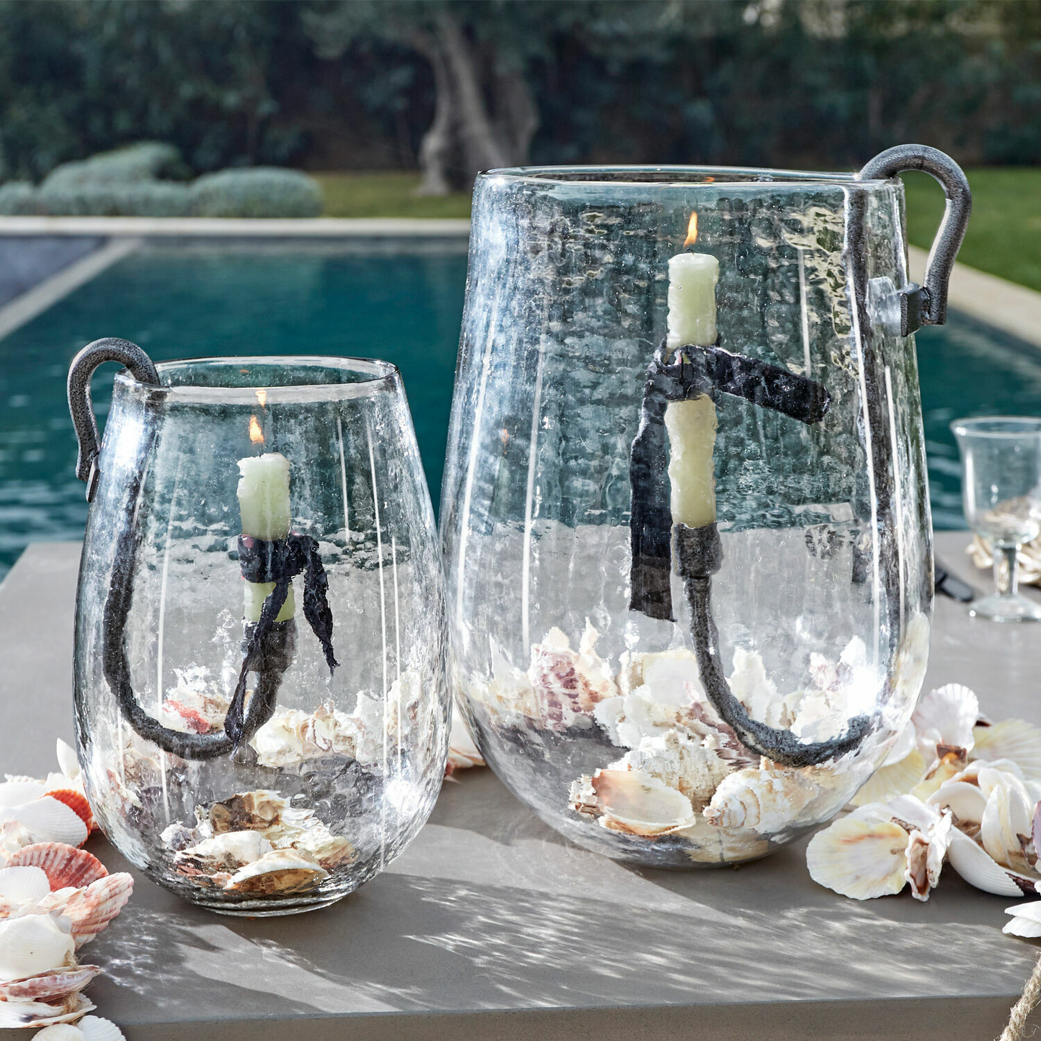Glazen lantaarns met metalen handvat en witte kaars, gevuld met schelpen, buitendecoratie