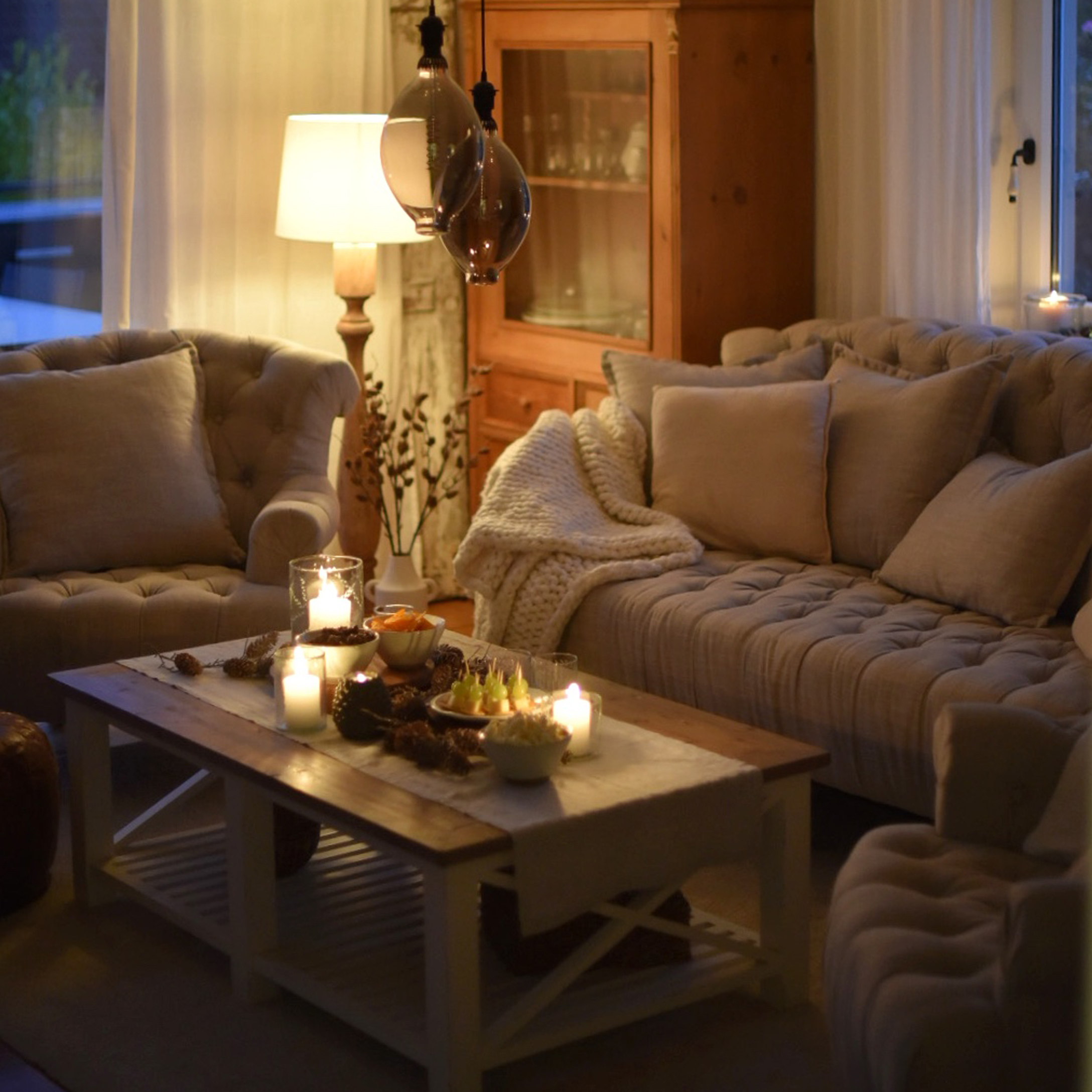 Gezellige woonkamer met beige bank, fauteuils en houten salontafel met kaarsen en snacks