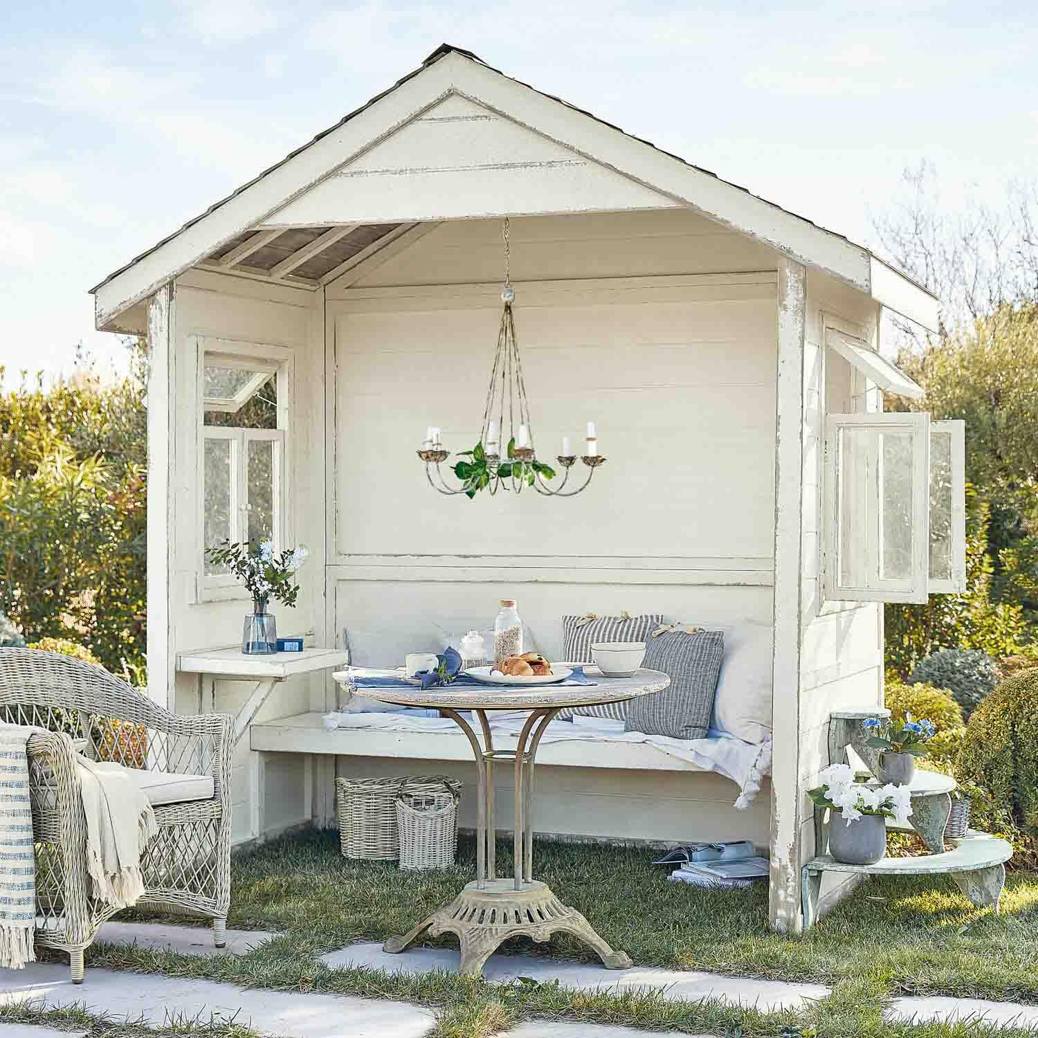 Witte houten tuinpaviljoen met rotan stoel en ronde tafel op gras