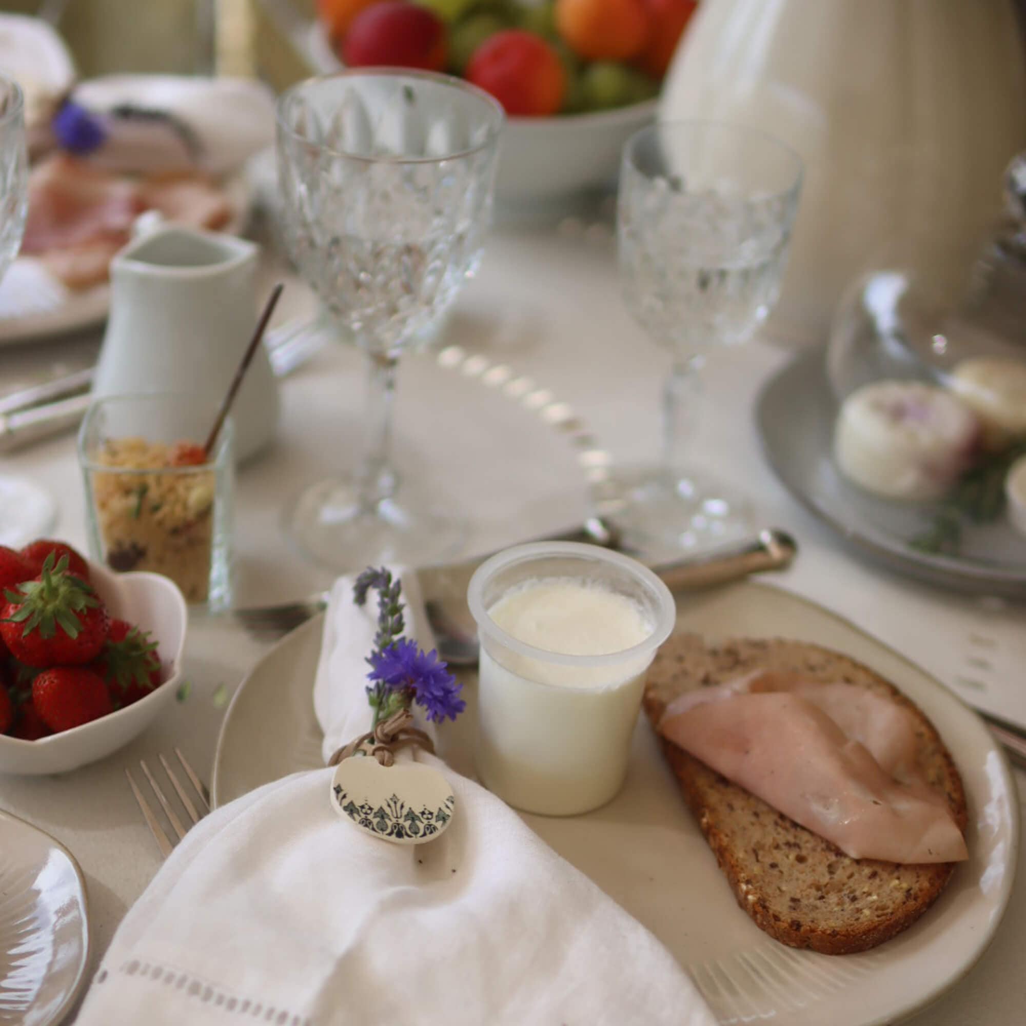 Ontbijttafel met volkorenbrood, ham en yoghurt op bord, servet met bloemdecoratie